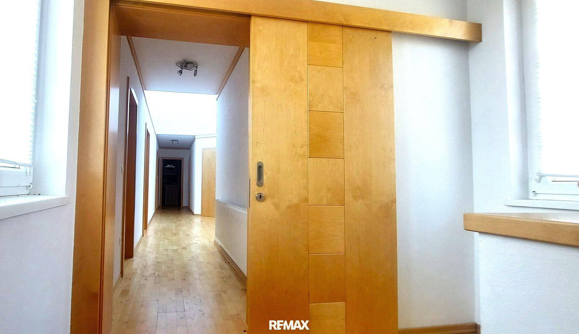 Heller Flur mit Holzfußboden und einer modernen Holzschiebetür, die zu weiteren Räumen führt.
