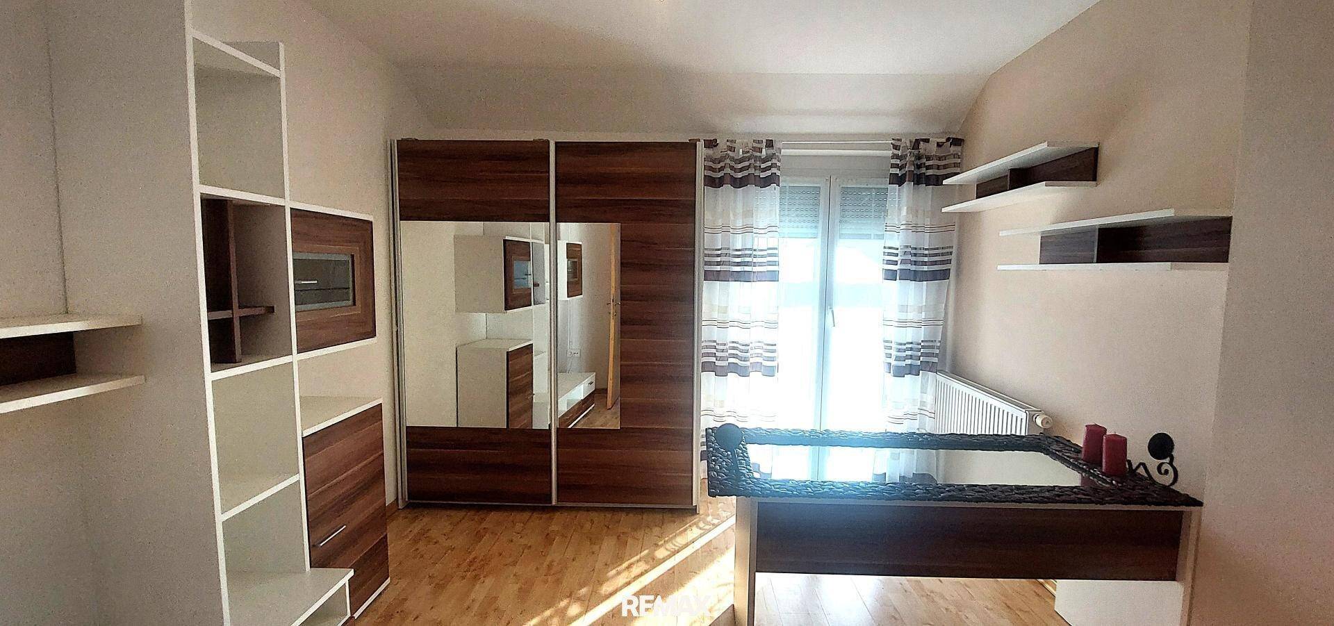 Schlafzimmer mit Holzboden, großem Spiegelschrank und Fenster mit Jalousien für Privatsphäre.