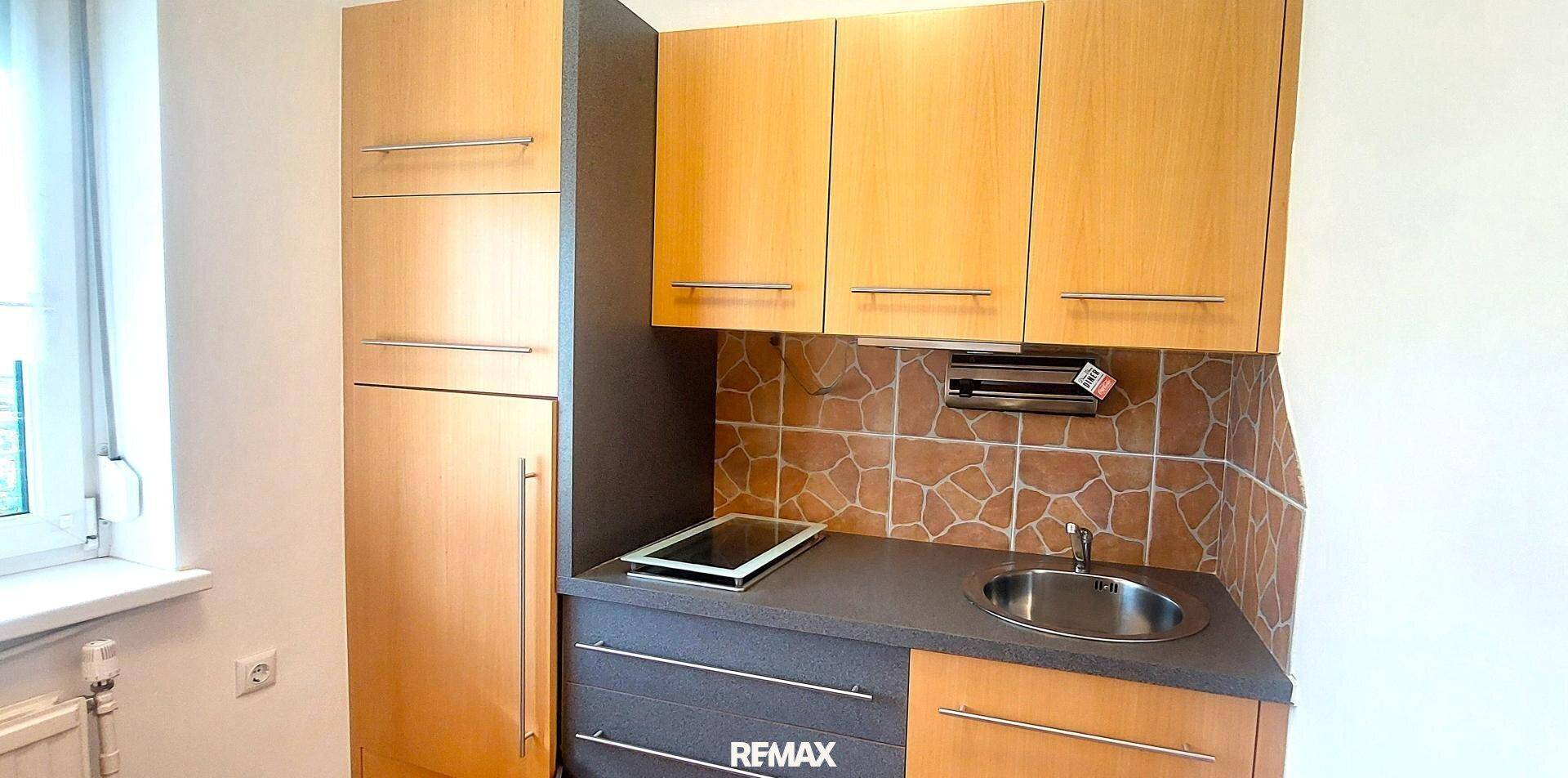 Kompakte Küchenzeile mit Holzschränken, Spüle, Kochfeld und integriertem Kühlschrank.