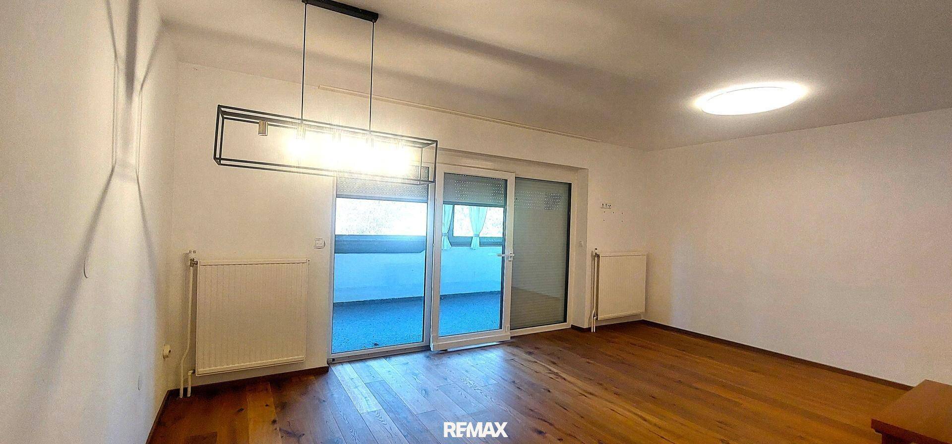 Helles Wohnzimmer mit Holzboden und großen Glasschiebetüren, die auf einen Balkon führen.