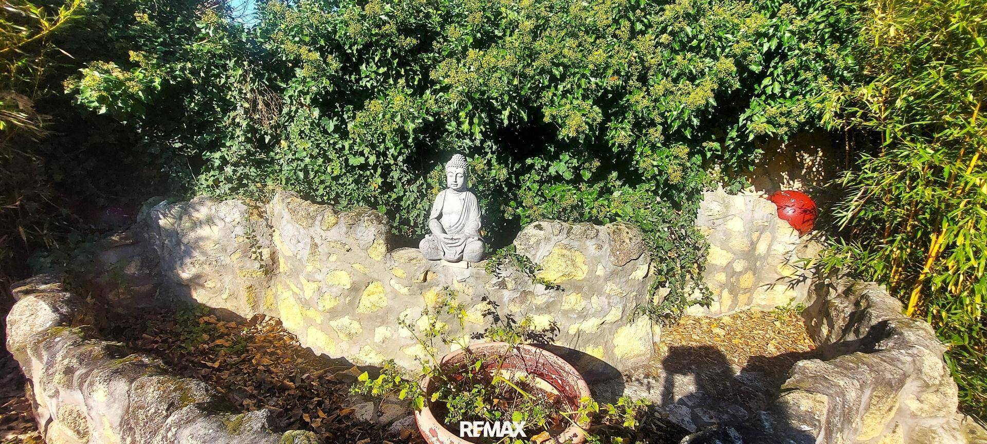 Dekorative Buddha-Statue in einer Steineinfassung im grünen Gartenbereich des Anwesens.