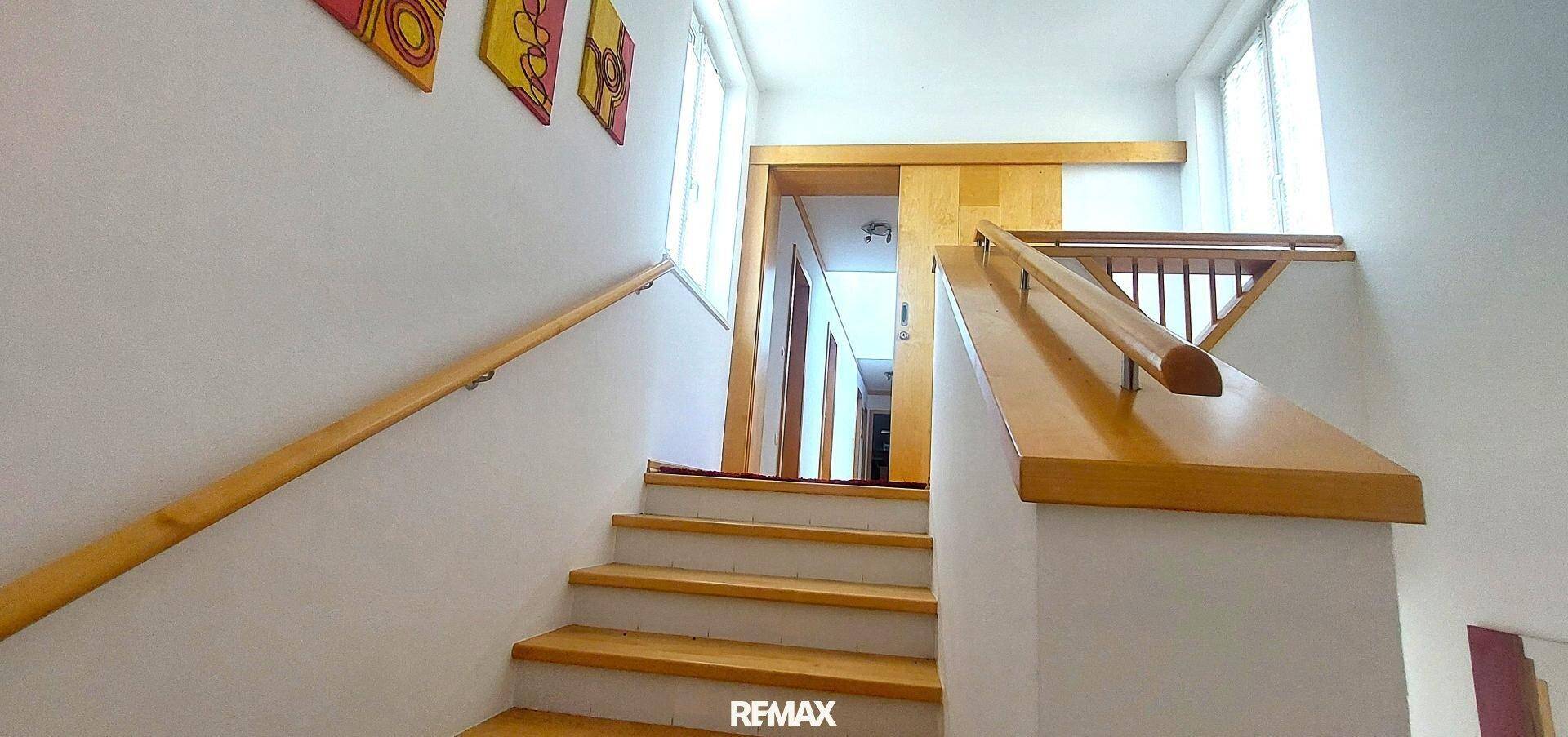 Holztreppe mit passendem Geländer und heller Wandgestaltung, die in die obere Etage führt.