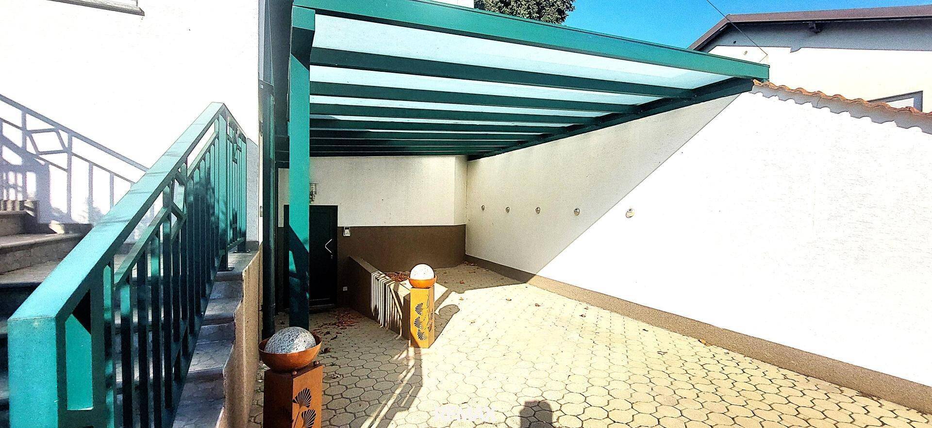 Überdachter Außenparkplatz oder Carport mit grünem Dach und gepflastertem Boden.