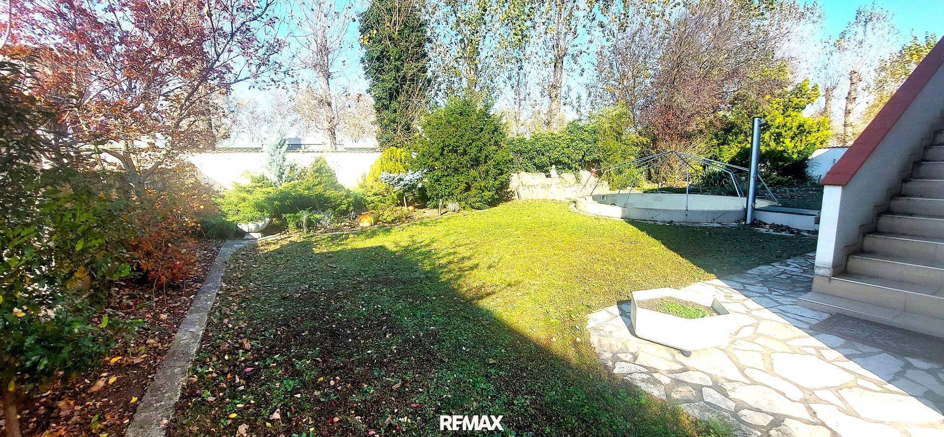 Weitläufiger Gartenbereich mit Rasenfläche, Bäumen und einem gepflasterten Weg zum Haus.