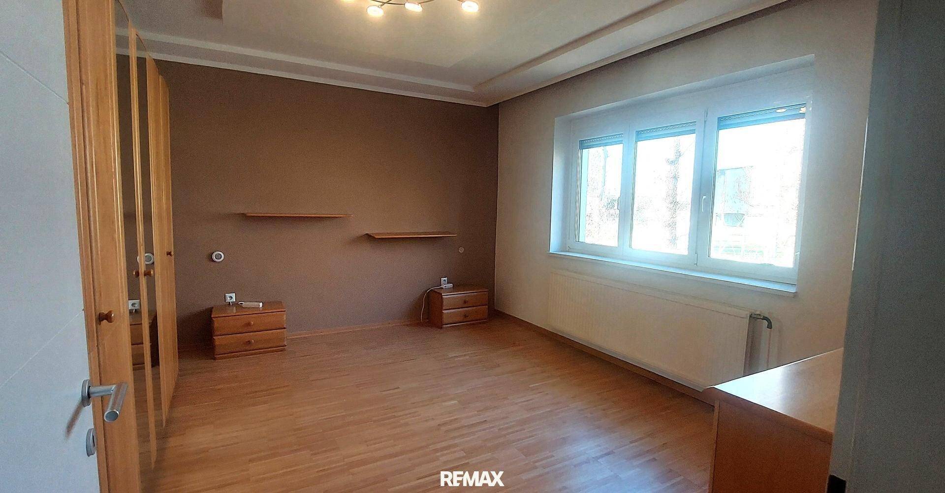 Geräumiges Schlafzimmer mit Holzboden, braunen Wänden und einem großen Fenster für viel Licht.