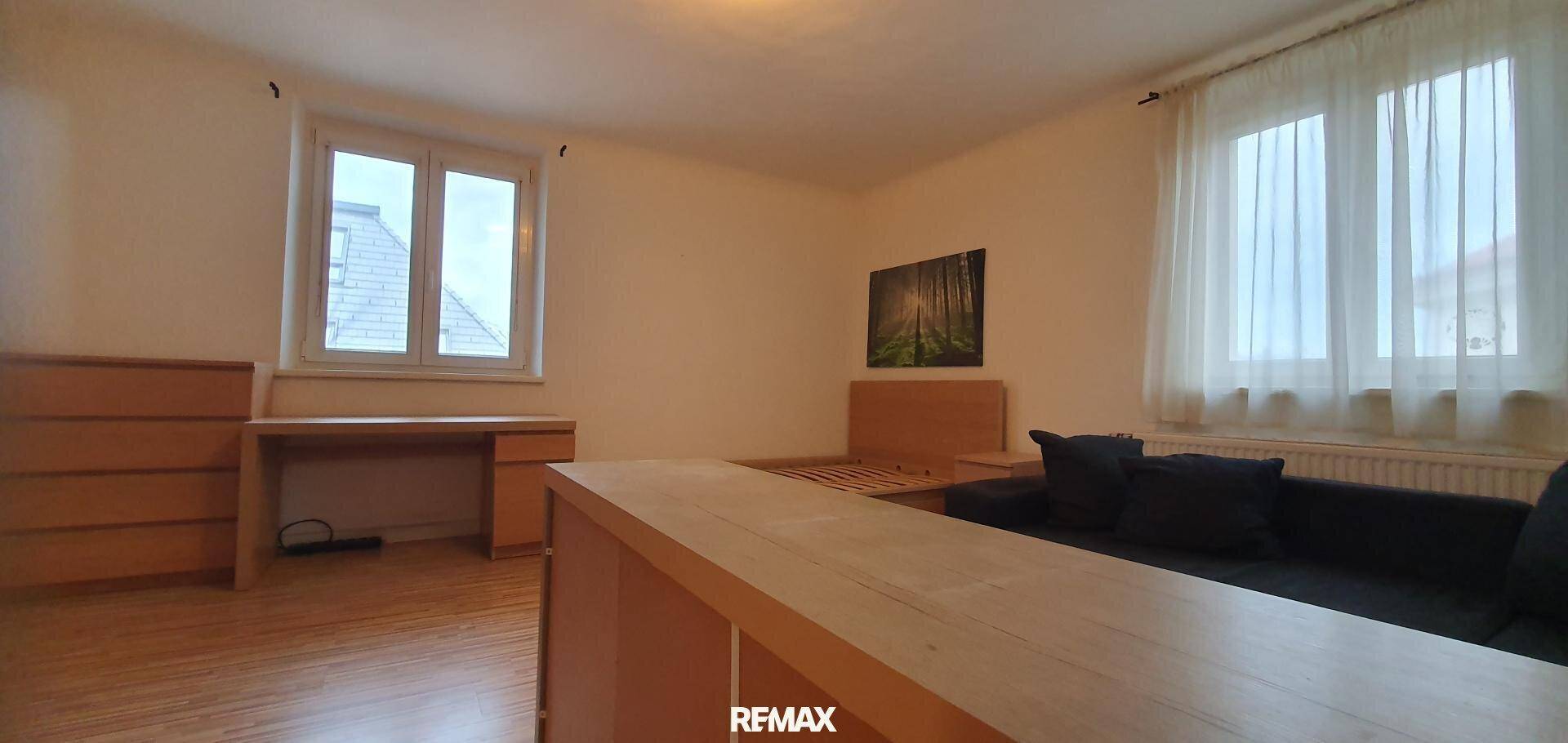 Geräumiges Zimmer mit zwei Fenstern, Holzboden und Platz für Schlaf- und Arbeitsbereich.
