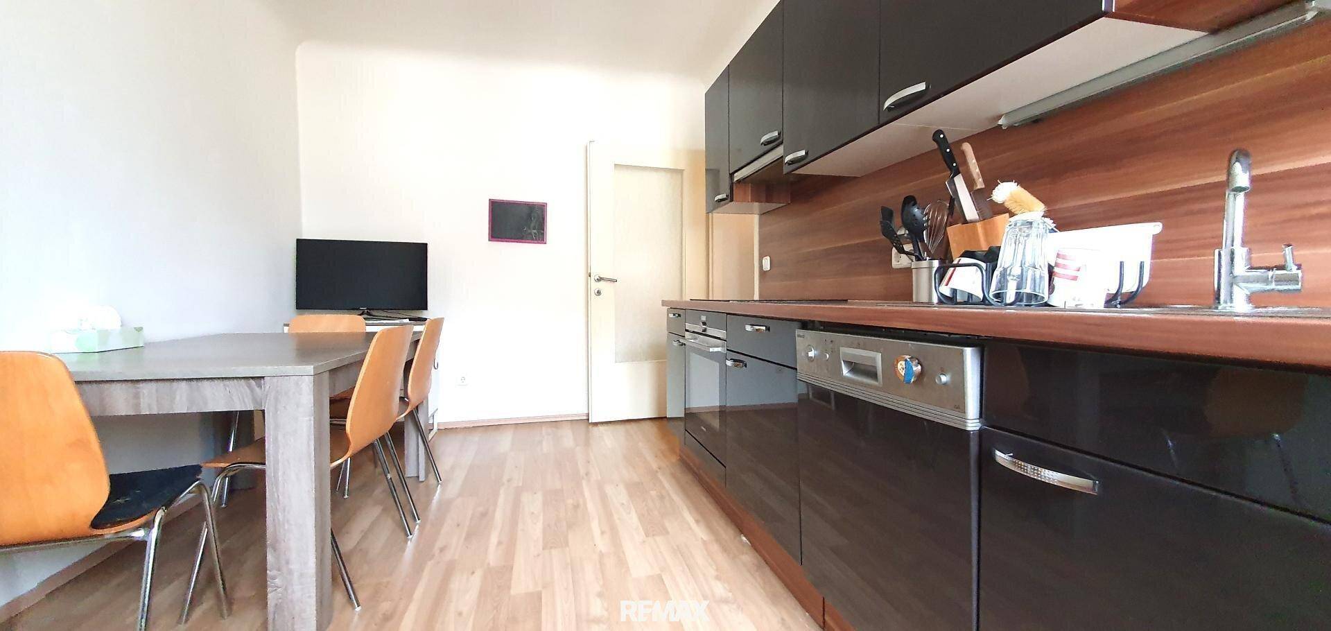 Moderne Einbauküche mit schwarzen Hochglanzfronten, integriertem Geschirrspüler und Essbereich.