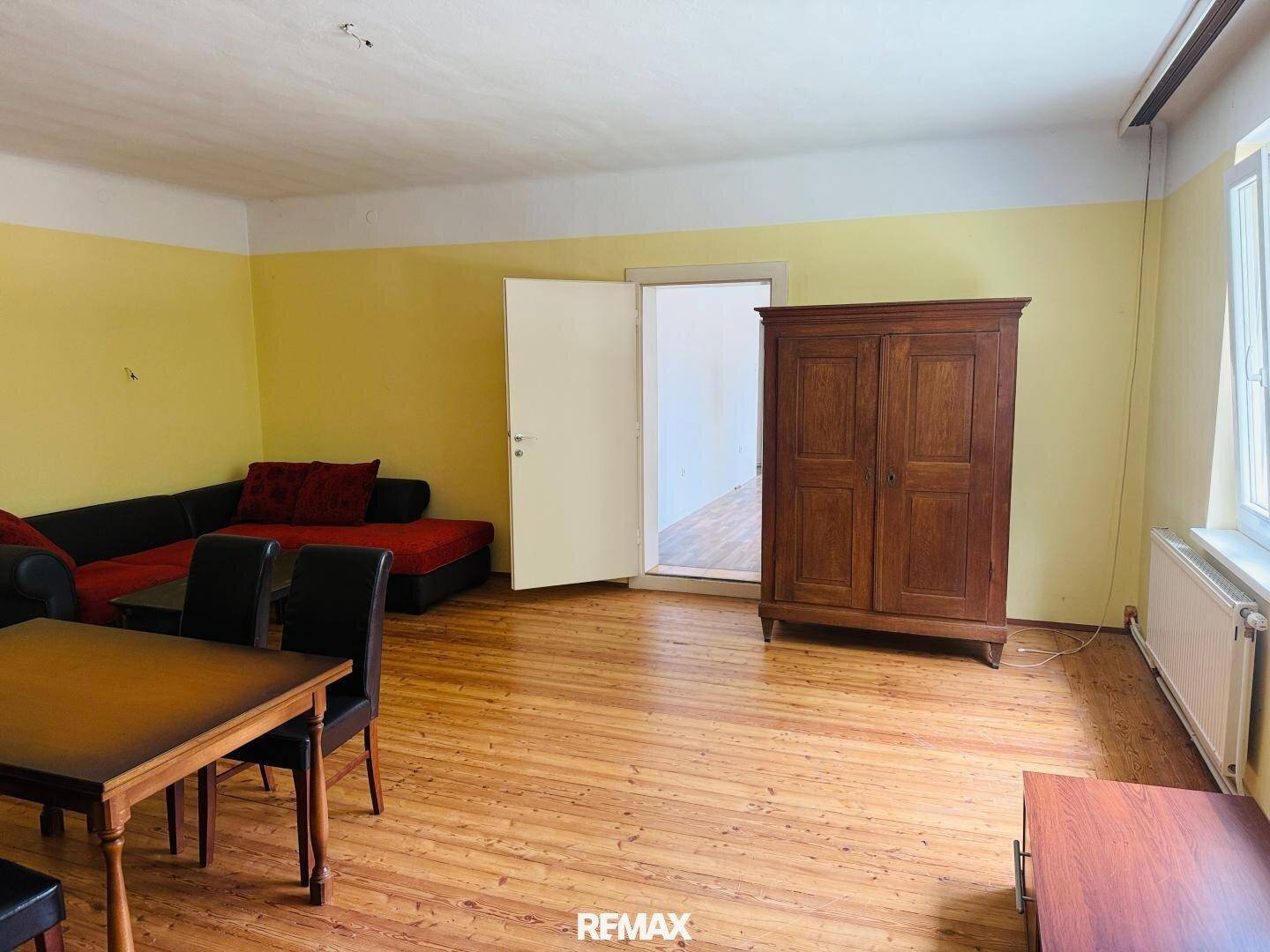 Wohn- und Esszimmer mit gelben Wänden, Laminatboden, einem Sofa und einem Esstisch.