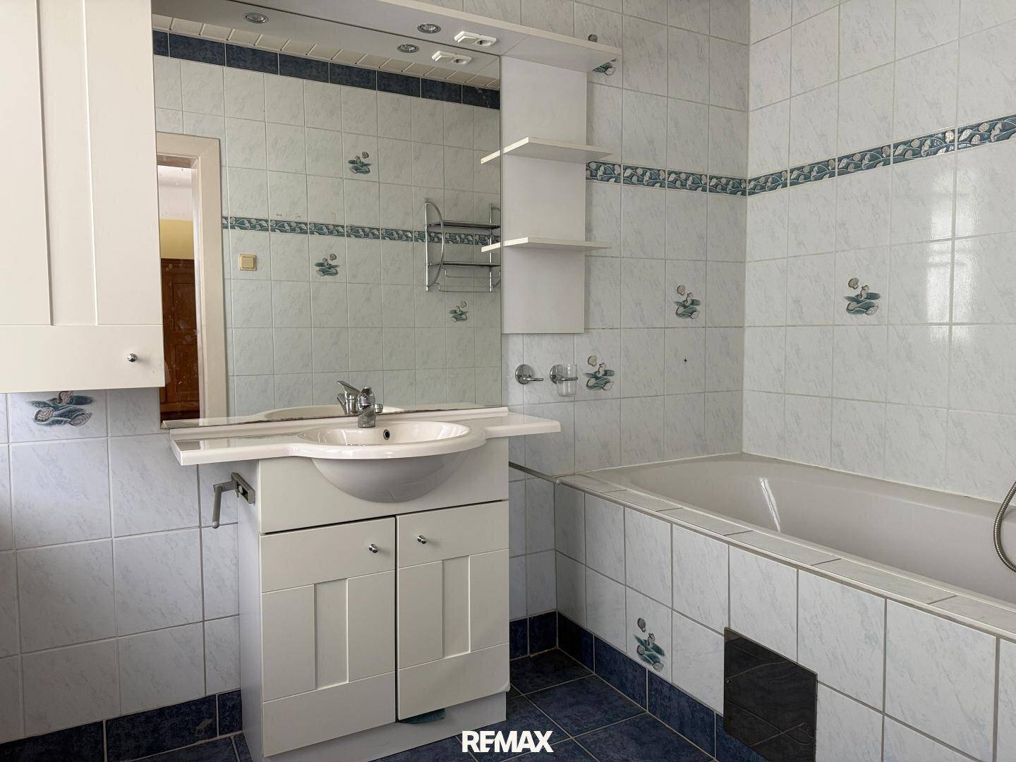 Badezimmer mit blau-weißen Fliesen, einer Badewanne und einem Waschtisch mit Spiegel.