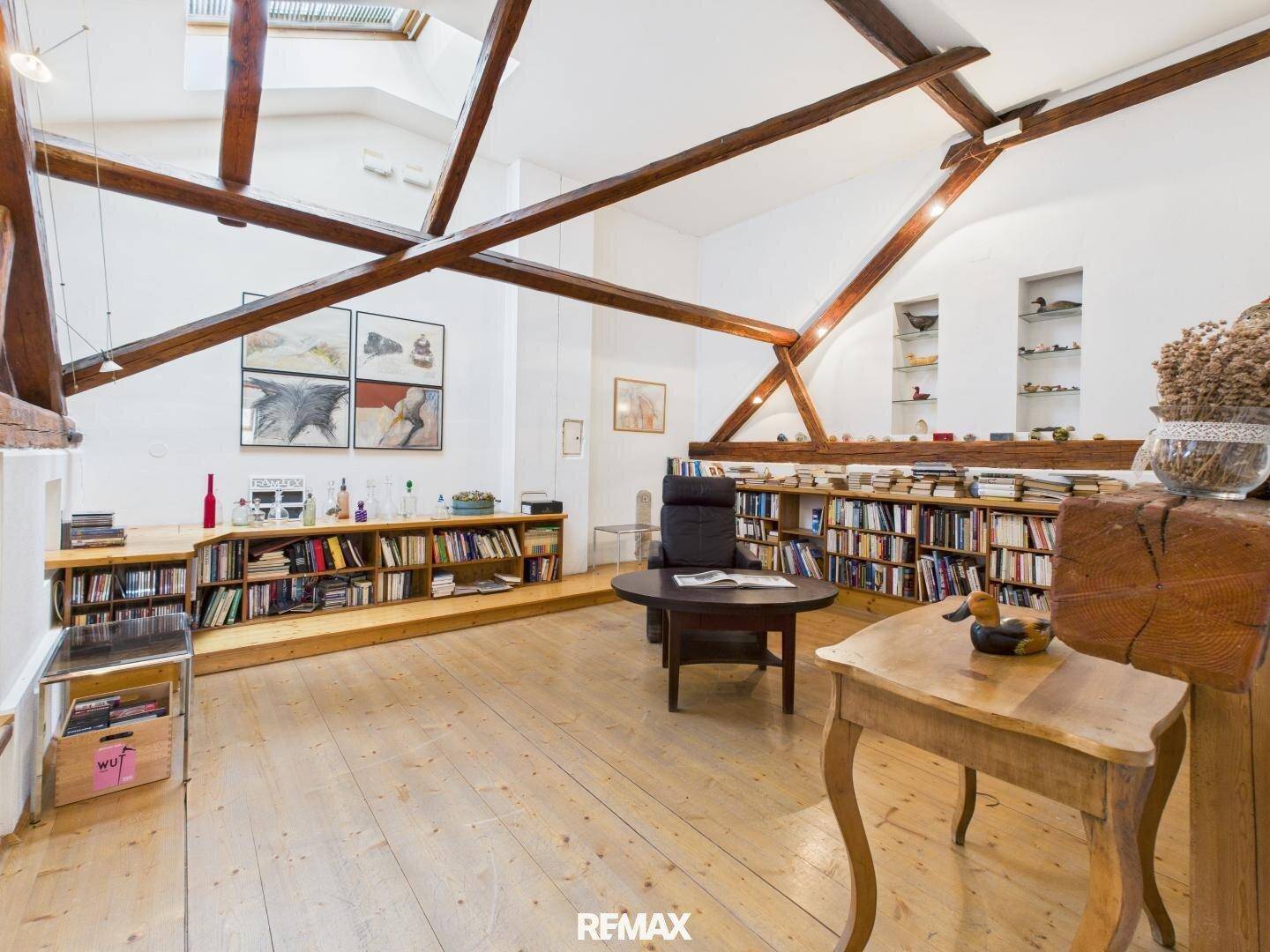 Gemütlicher Wohnbereich im Dachgeschoss mit Holzbalken, Bücherregalen und Oberlichtern, schafft eine helle Atmosphäre.