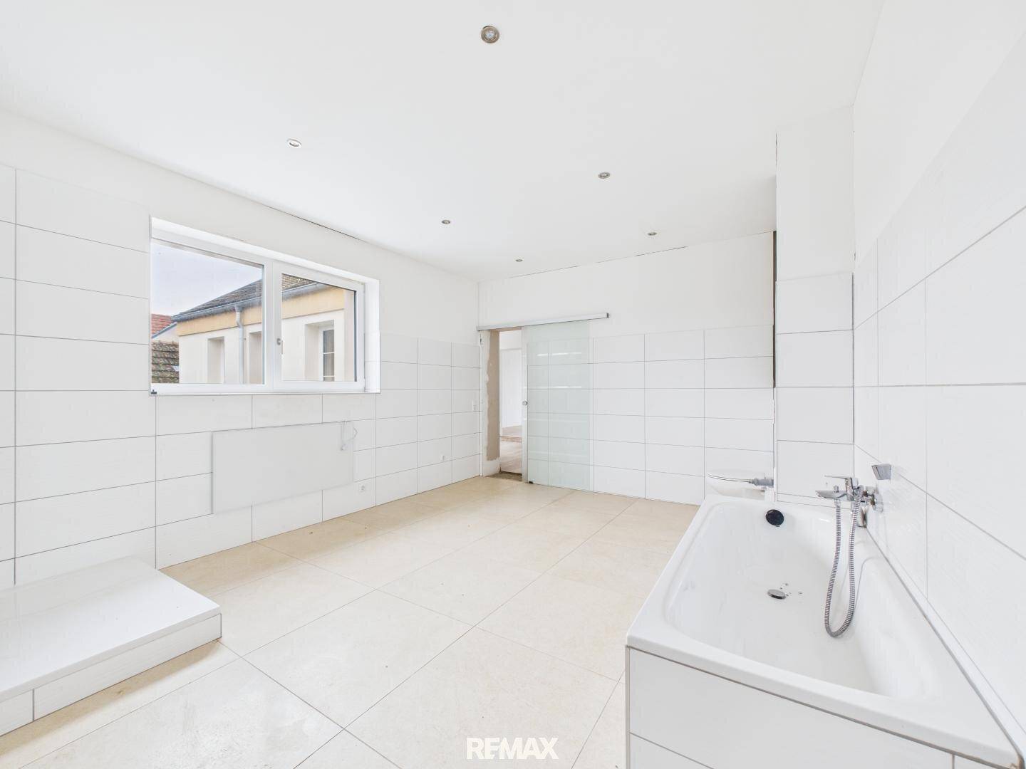 Unfertiges Badezimmer mit Badewanne, weißen Fliesen und Schiebetür, bietet viel Gestaltungspotenzial.