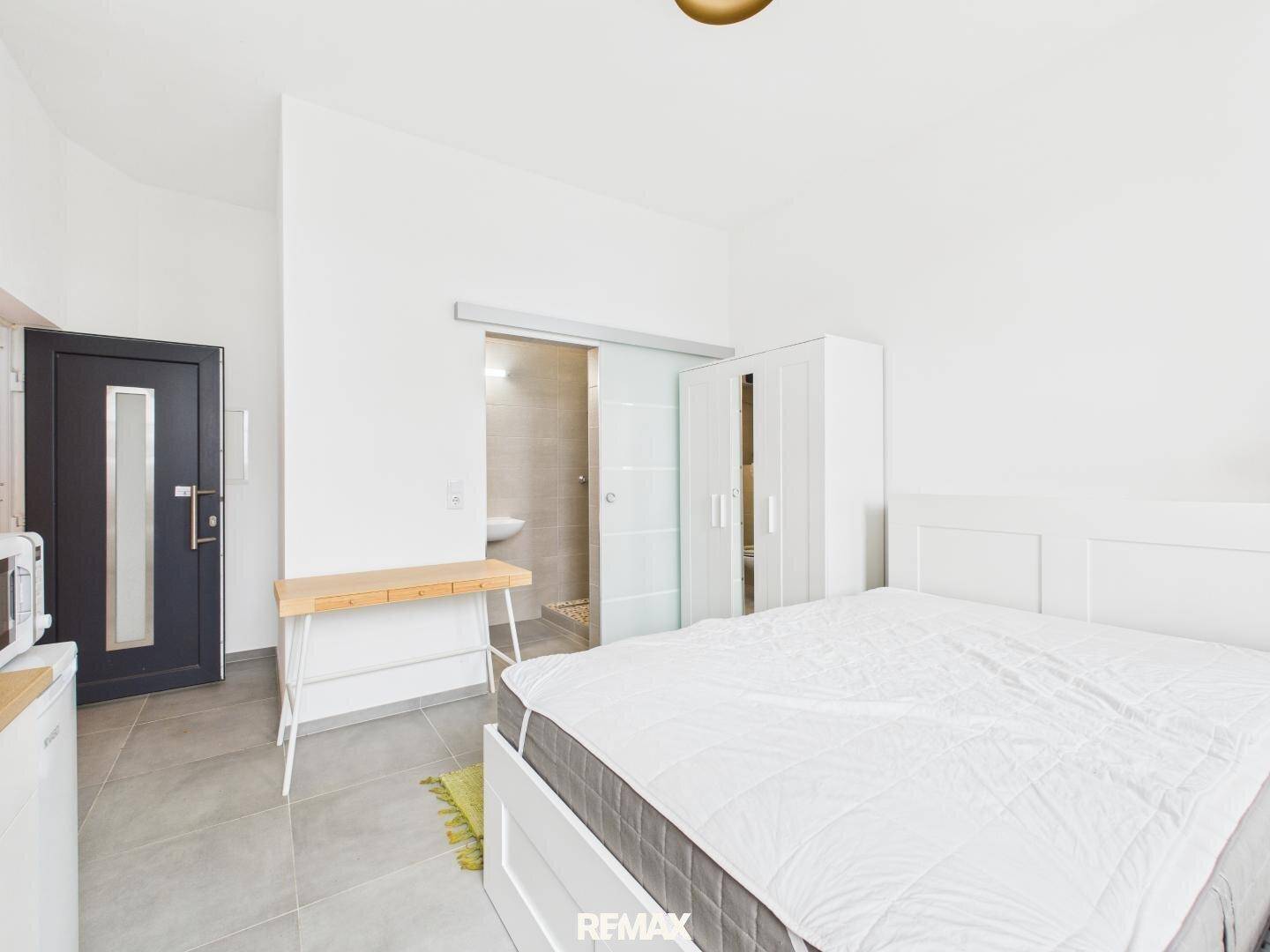Modernes Schlafzimmer mit Doppelbett, Schiebetür zum Bad und grauen Fliesenboden, sehr funktional.