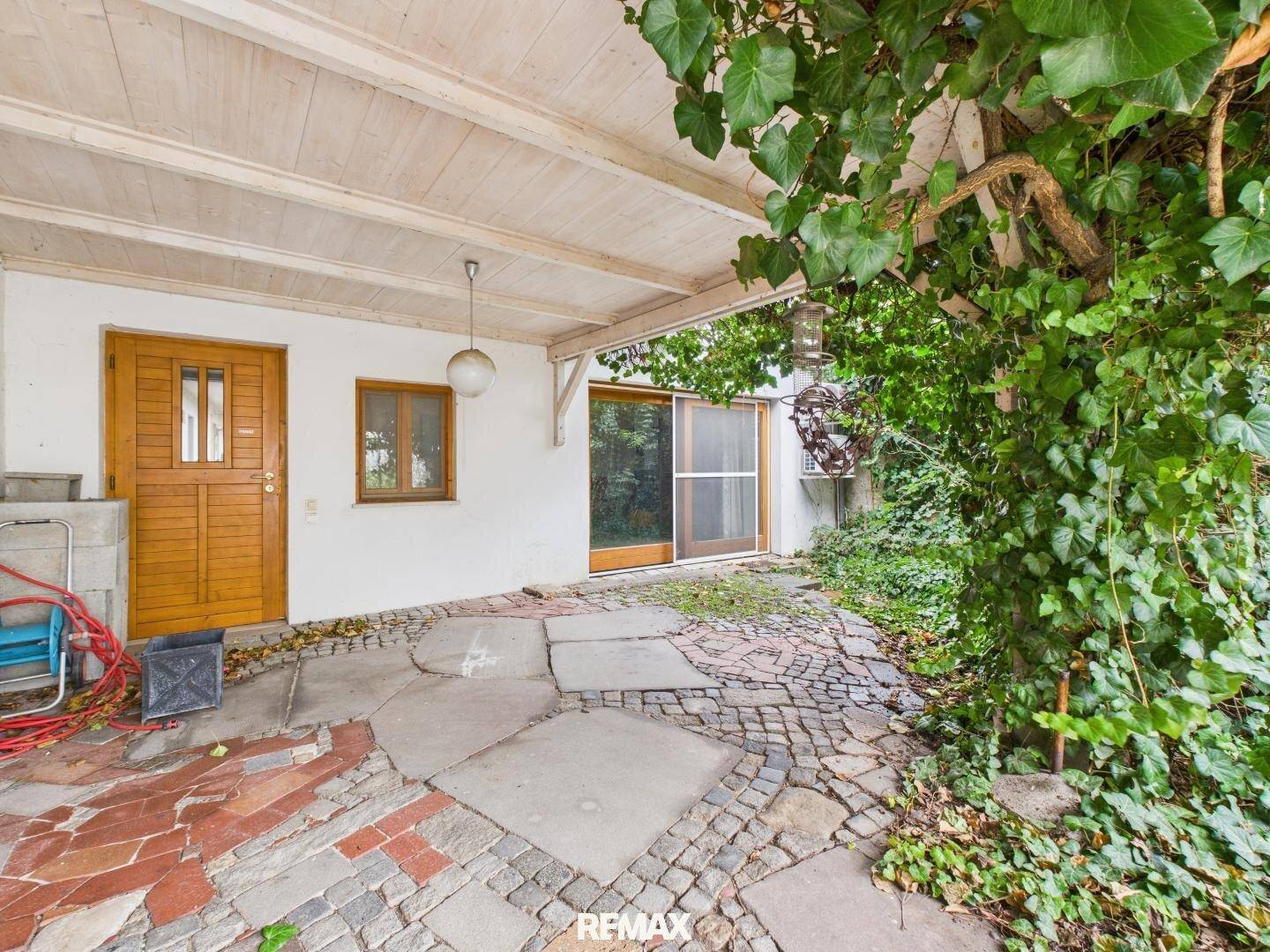 Überdachte Terrasse mit Steinplatten und üppiger Begrünung, ideal für entspannte Stunden im Freien.