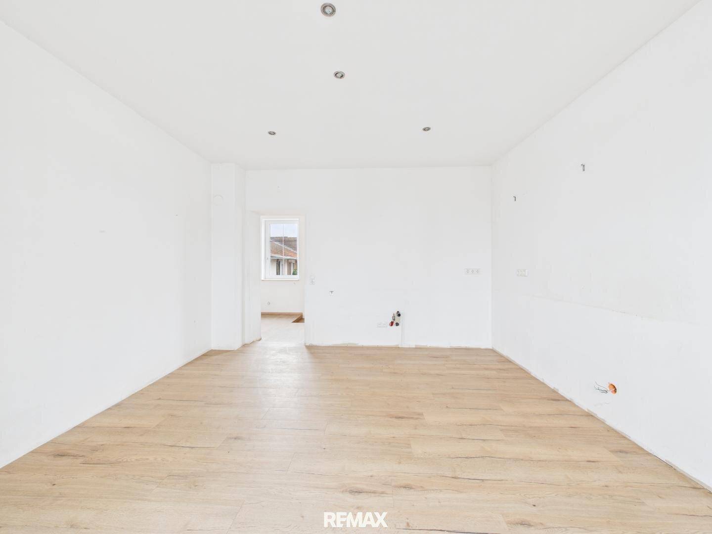 Heller, unfertiger Raum mit Holzboden und einem Fenster, bereit für den individuellen Innenausbau.