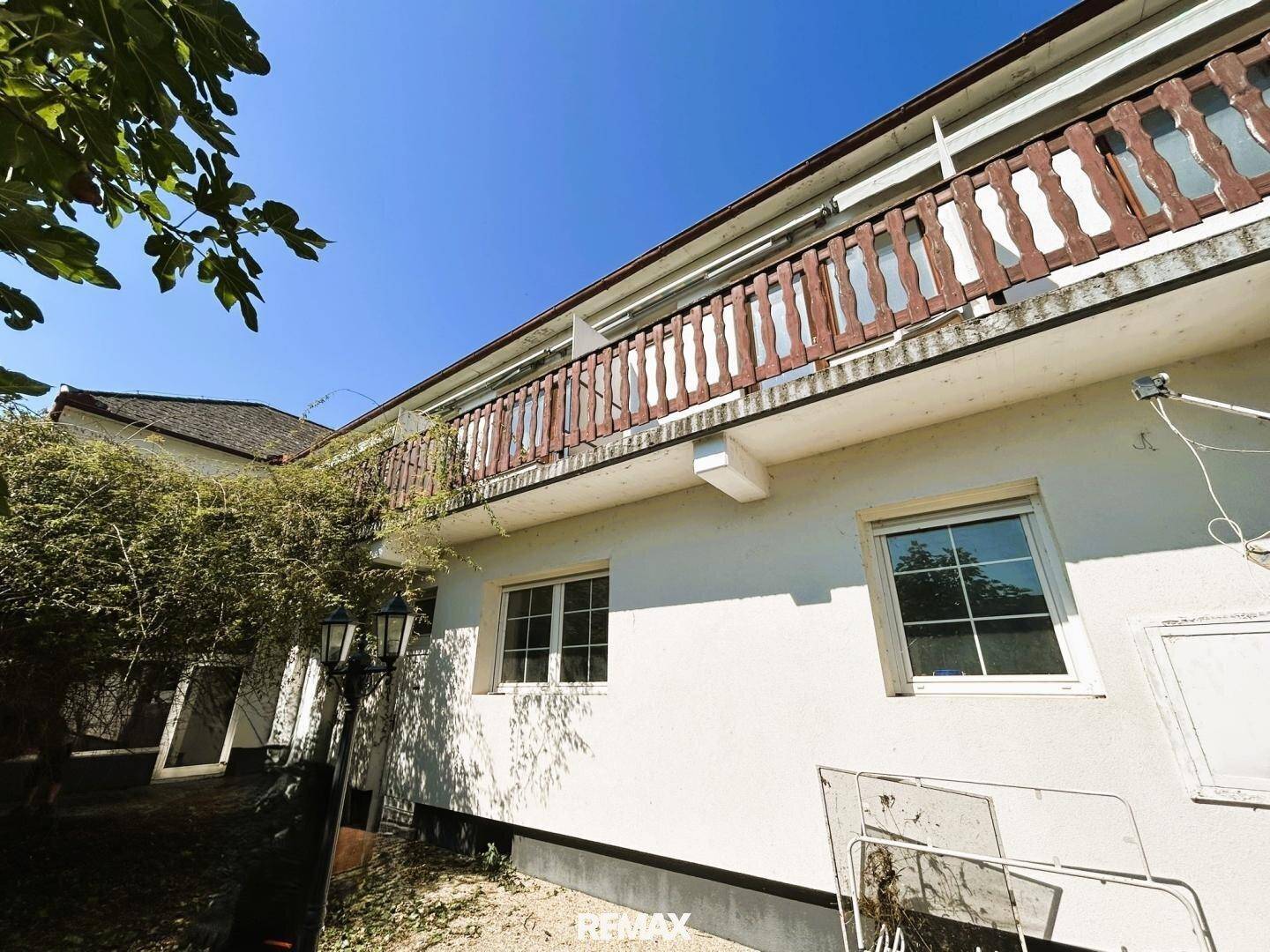 Fassade eines Gebäudes mit einem langen Balkon und traditionellem Holzgeländer unter blauem Himmel.