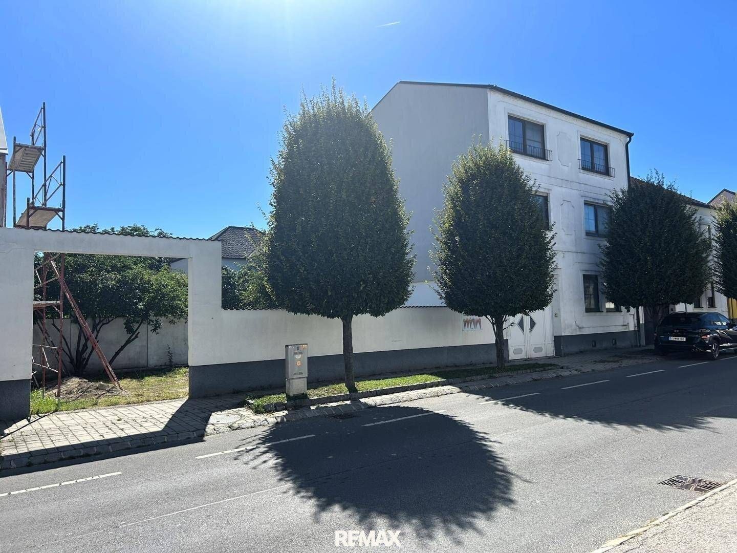 Außenansicht eines Gebäudes an der Straße mit einem angrenzenden leeren Grundstück und Bäumen.