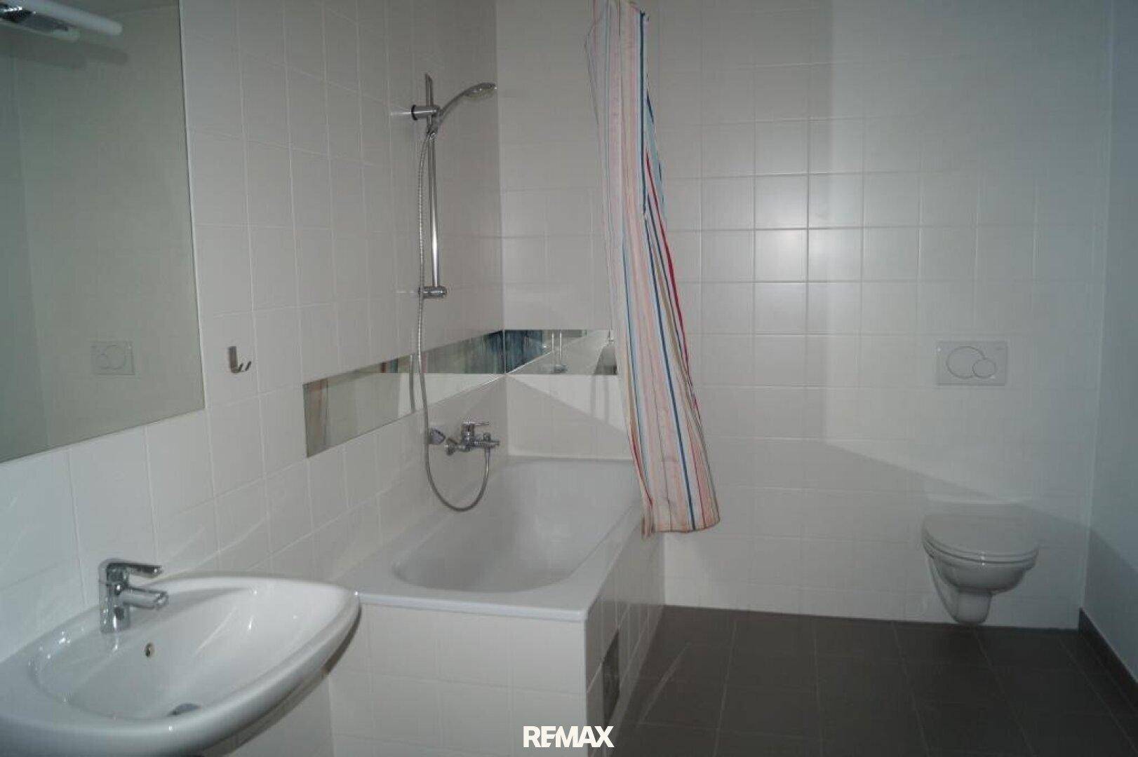 Funktionales Badezimmer mit Badewanne, Dusche, WC und Waschbecken, komplett weiß gefliest.