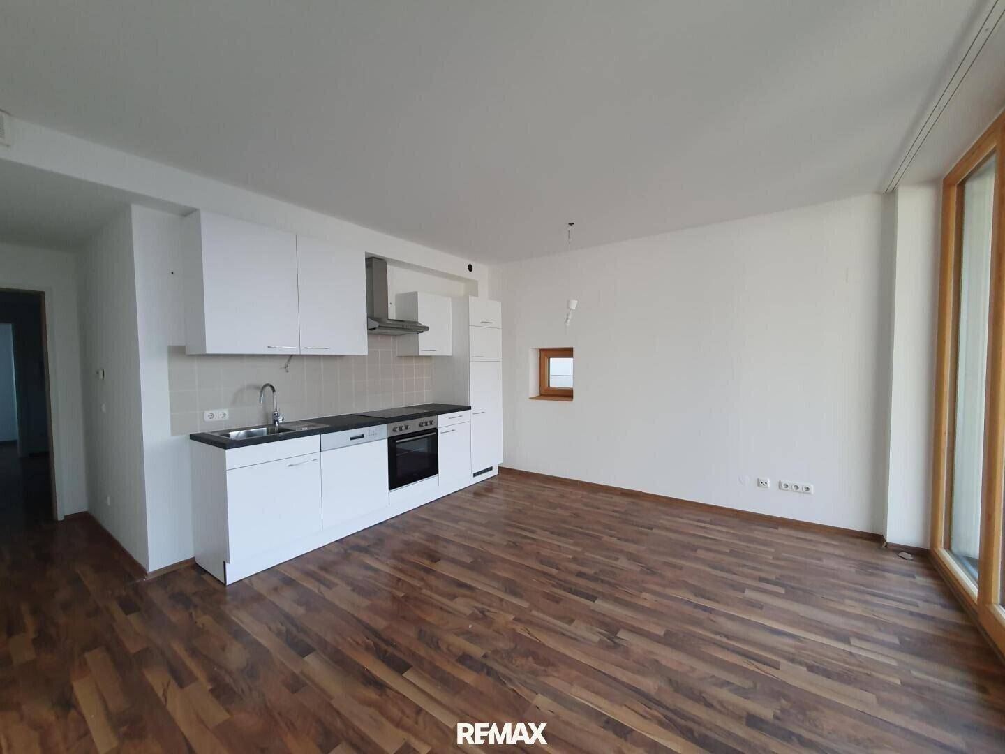 Offener Wohnbereich mit integrierter Küchenzeile, Holzboden und Fenster für natürliches Licht.