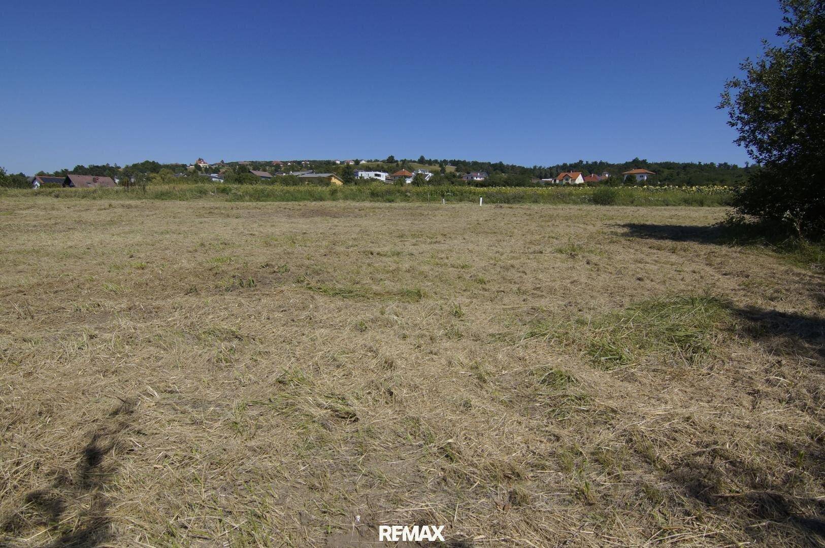 Weitläufiges Feld mit trockenem Gras und einem Panoramablick auf die hügelige Landschaft mit Häusern.