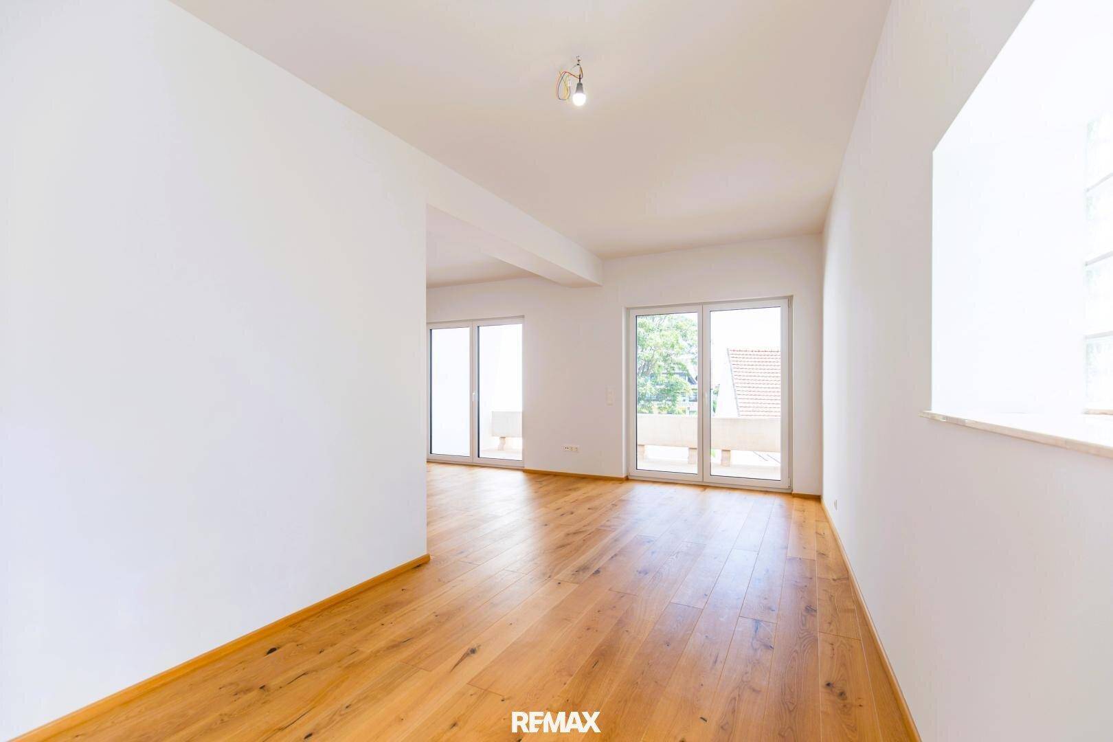 Heller Wohnraum mit Holzboden und großen Fenstern, die viel Tageslicht hereinlassen.