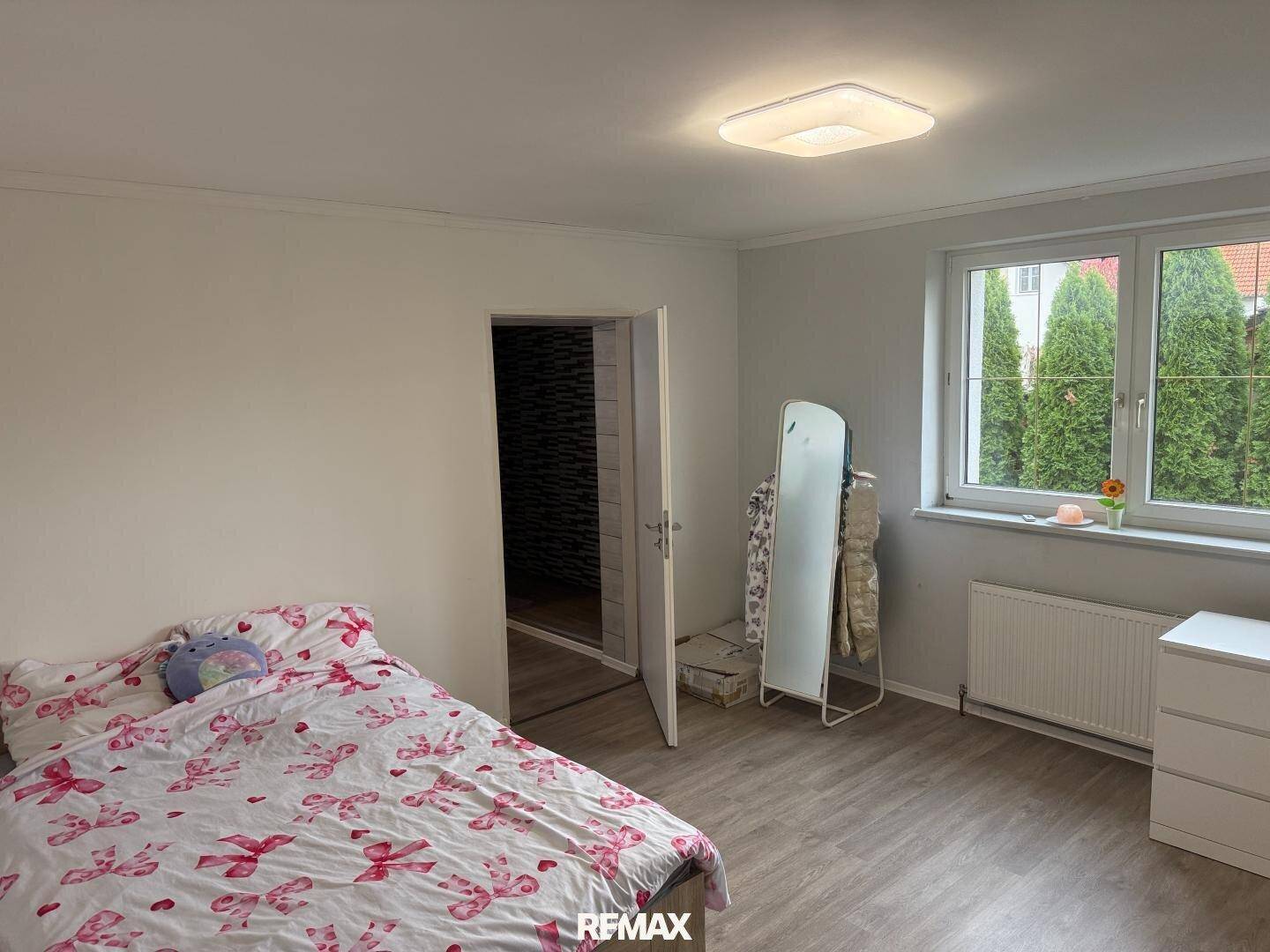 Helles Schlafzimmer mit Doppelbett, hellem Laminatboden und Blick ins Grüne.