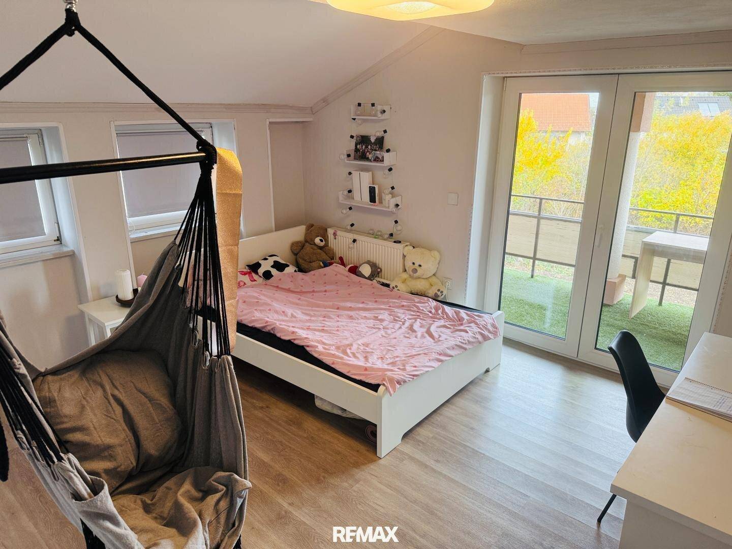 Kinderzimmer mit Bett, Hängesessel und Zugang zu einem kleinen Balkon.