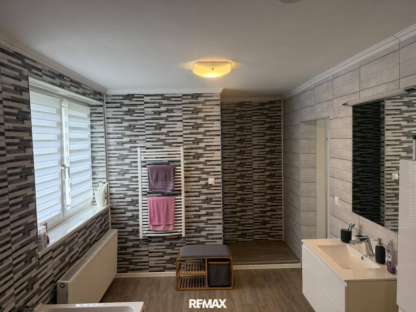 Modernes Badezimmer mit gemusterten Fliesen, Dusche, Badewanne und Doppelwaschbecken.