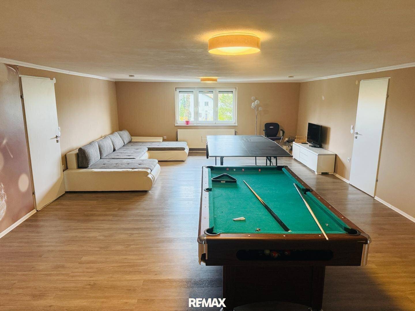 Geräumiger Spiel- und Freizeitraum mit Billardtisch, Tischtennisplatte und großem Sofa.