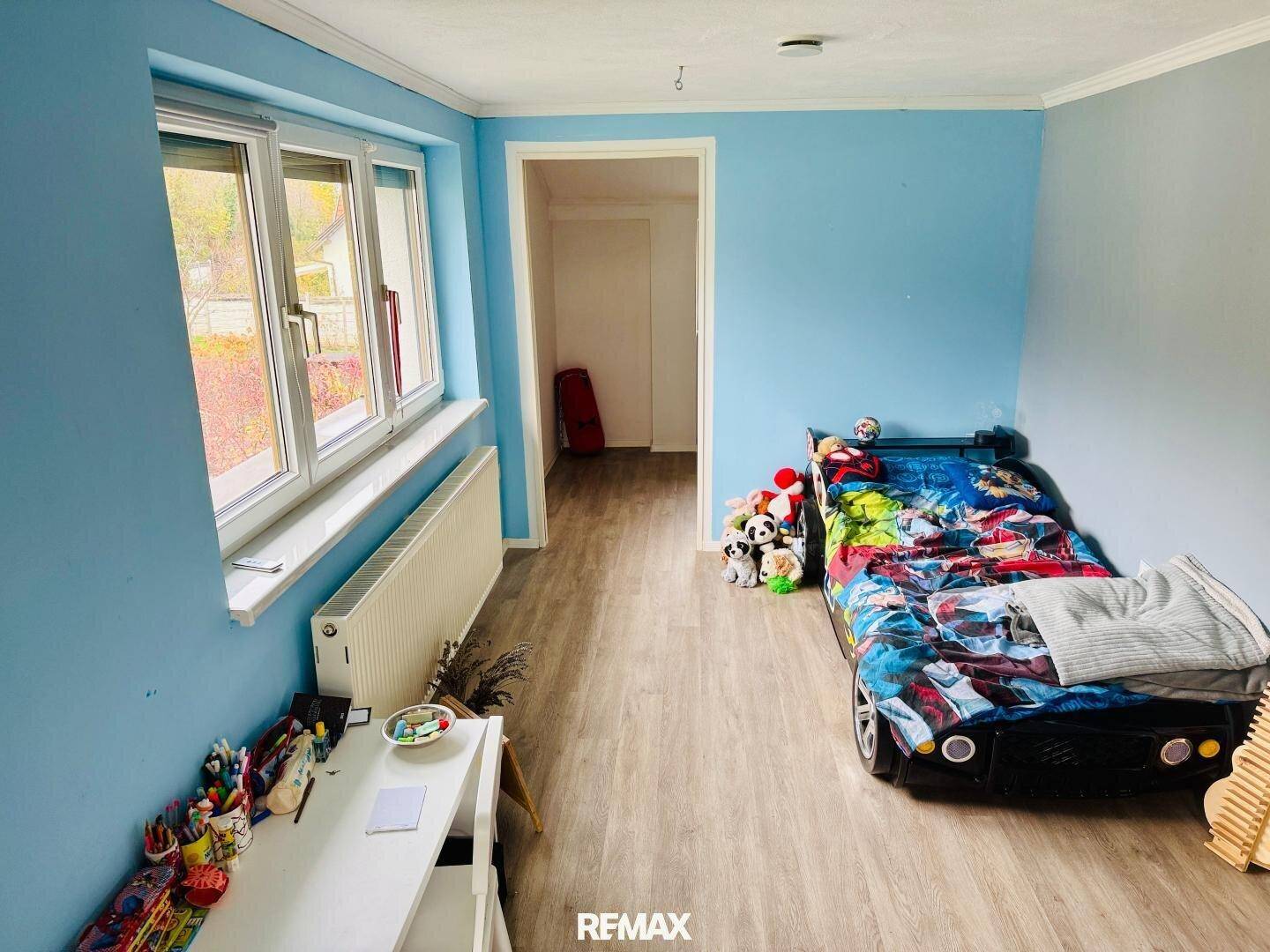 Kinderzimmer mit blau gestrichenen Wänden, Spielzeug und hellem Laminatboden.