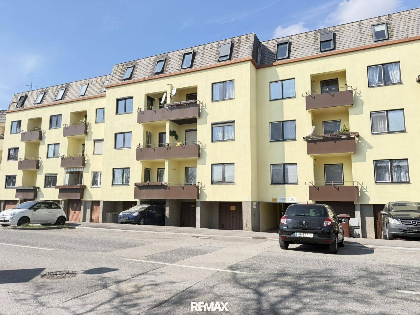 Mehrfamilienhaus mit gelber Fassade, mehreren Balkonen und Dachfenstern, an einer Straße gelegen.
