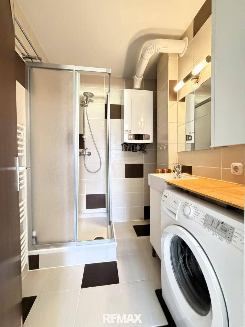 Funktionales Badezimmer mit Duschkabine, Waschmaschine und modernen Fliesen in Braun-Beige.