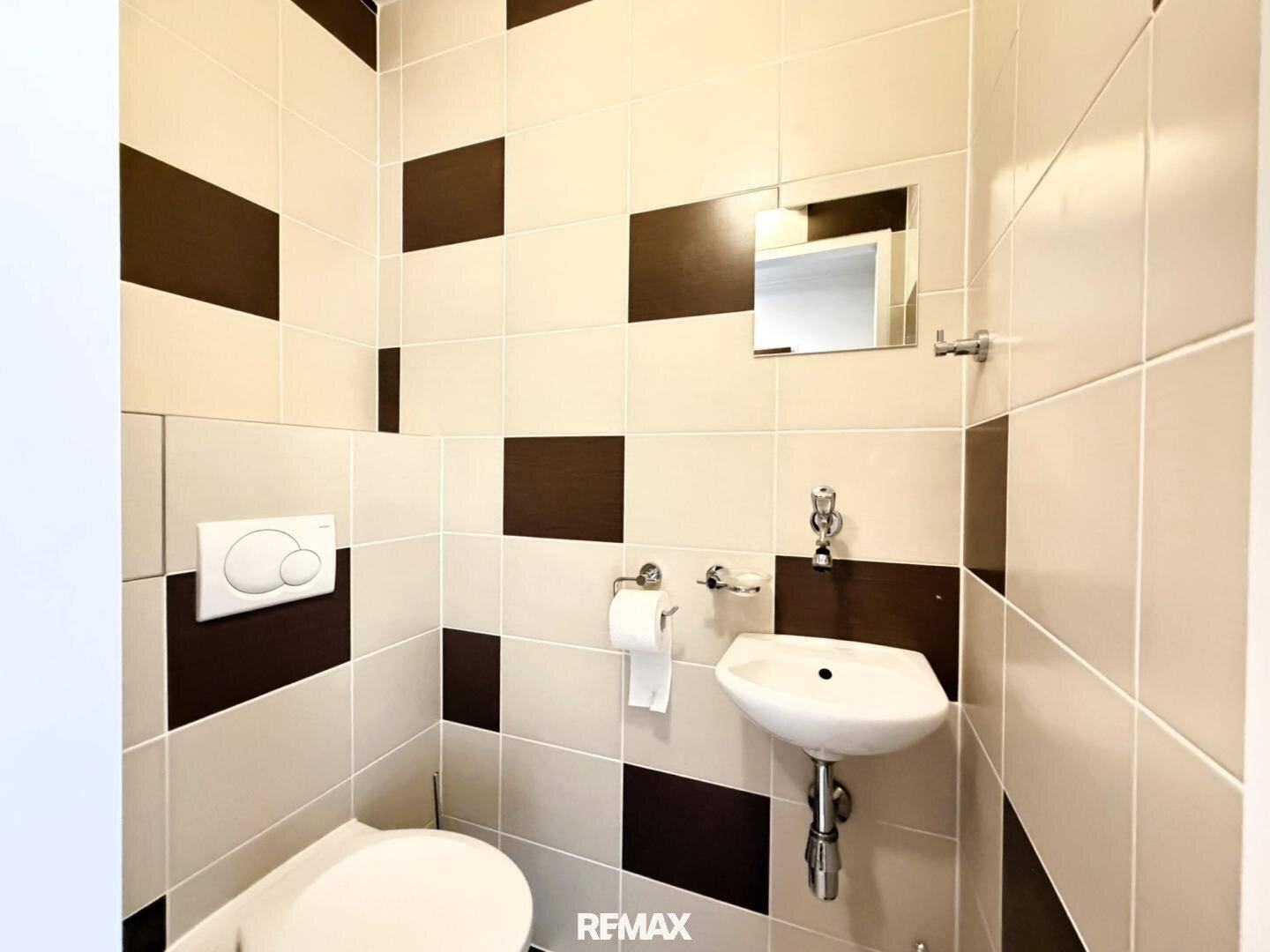 Kleines Gäste-WC mit Wand-WC und Handwaschbecken, gefliest in Braun-Beige-Tönen.