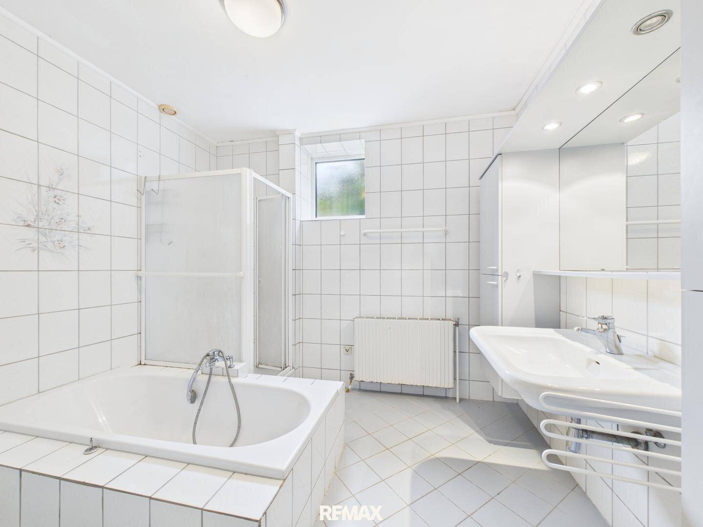 Gefliestes Badezimmer mit Badewanne, Dusche, Waschbecken und einem Fenster für natürliche Belüftung.