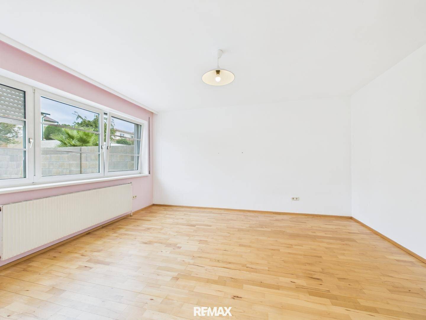Helles Schlafzimmer mit Holzboden, großen Fenstern und einer dezent rosa gestrichenen Wand.