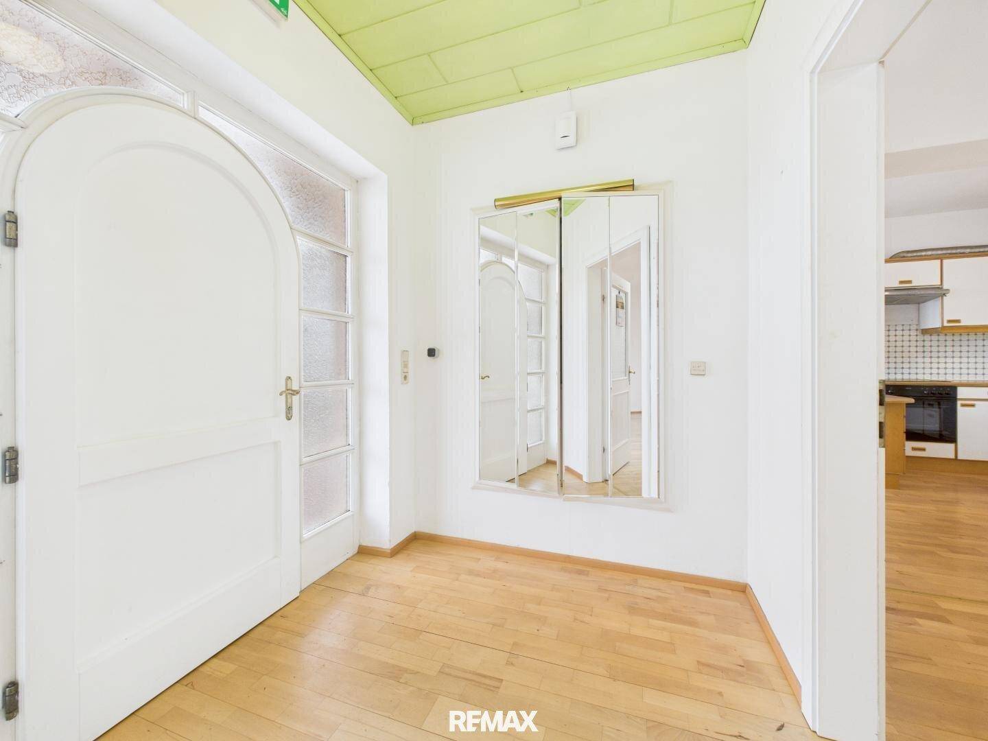 Heller Eingangsbereich mit Holzboden, weißer Tür und einem großen Spiegel an der Wand.