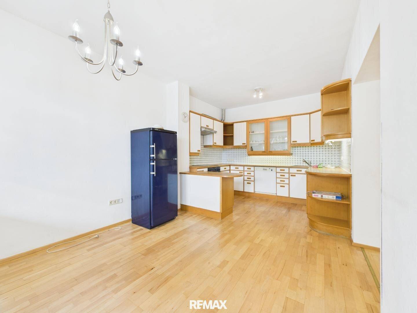 Küche mit Holzboden, weißen Schränken und einem auffälligen blauen Kühlschrank in einem offenen Raum.