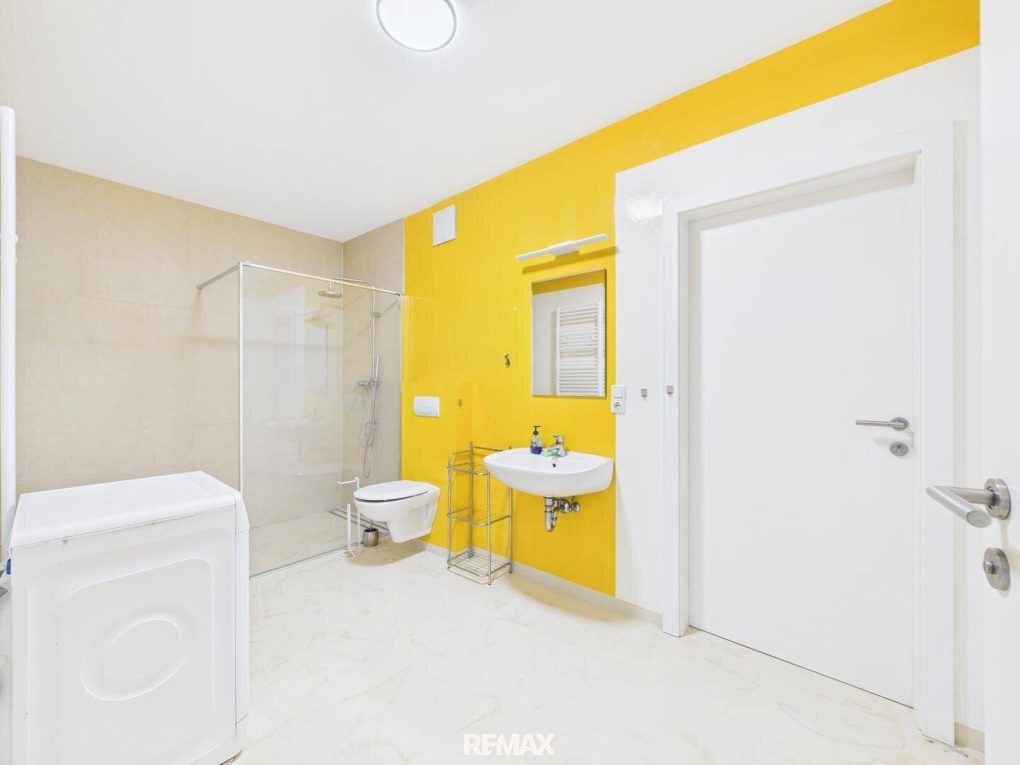 Modernes Badezimmer im Untergeschoss mit gelben Akzentwänden, Dusche und Waschmaschine.
