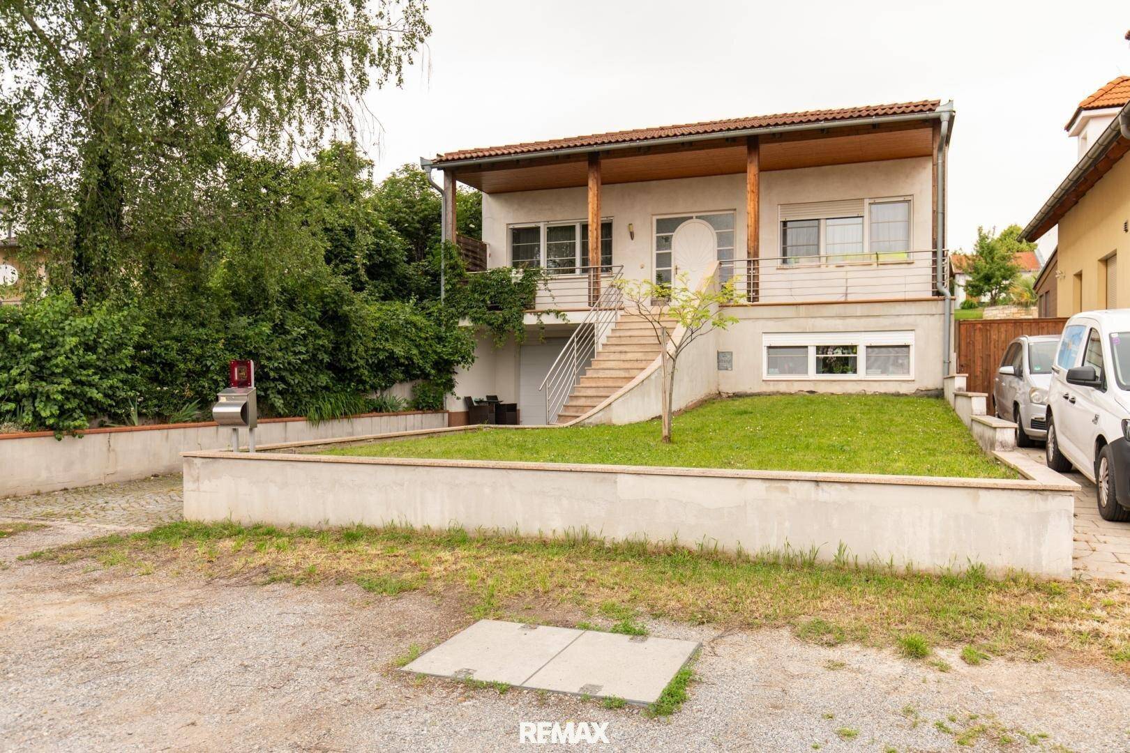 Seitenansicht des Hauses mit Außentreppe zum Eingang und Parkplätzen vor dem Gebäude.