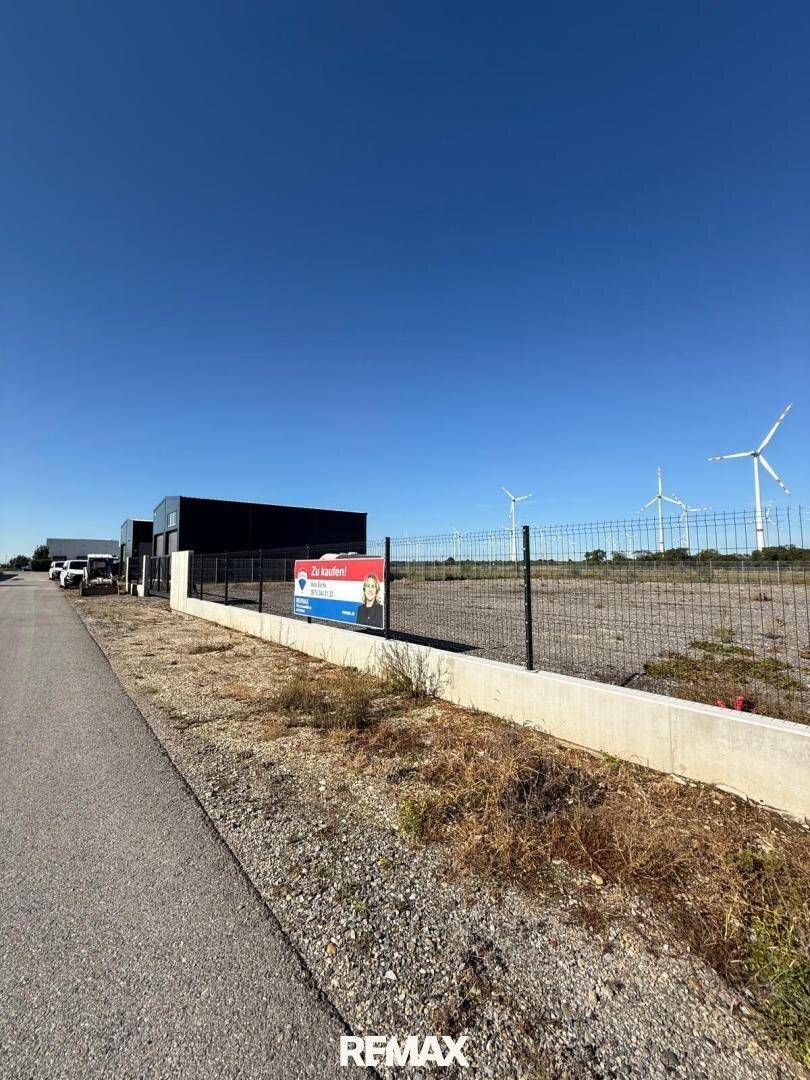 Weitläufiges Grundstück mit Zaun, einem Gebäude und Windkraftanlagen am Horizont.