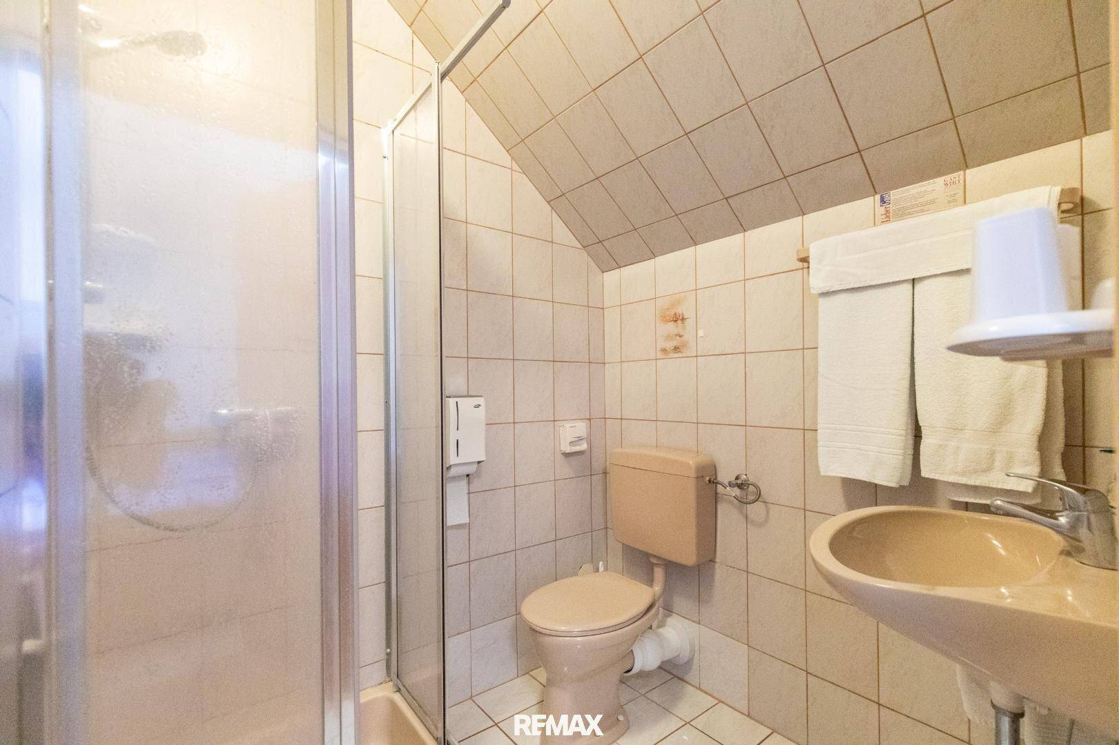Badezimmer mit Duschkabine, WC und Waschbecken, gefliest und mit Dachschräge.