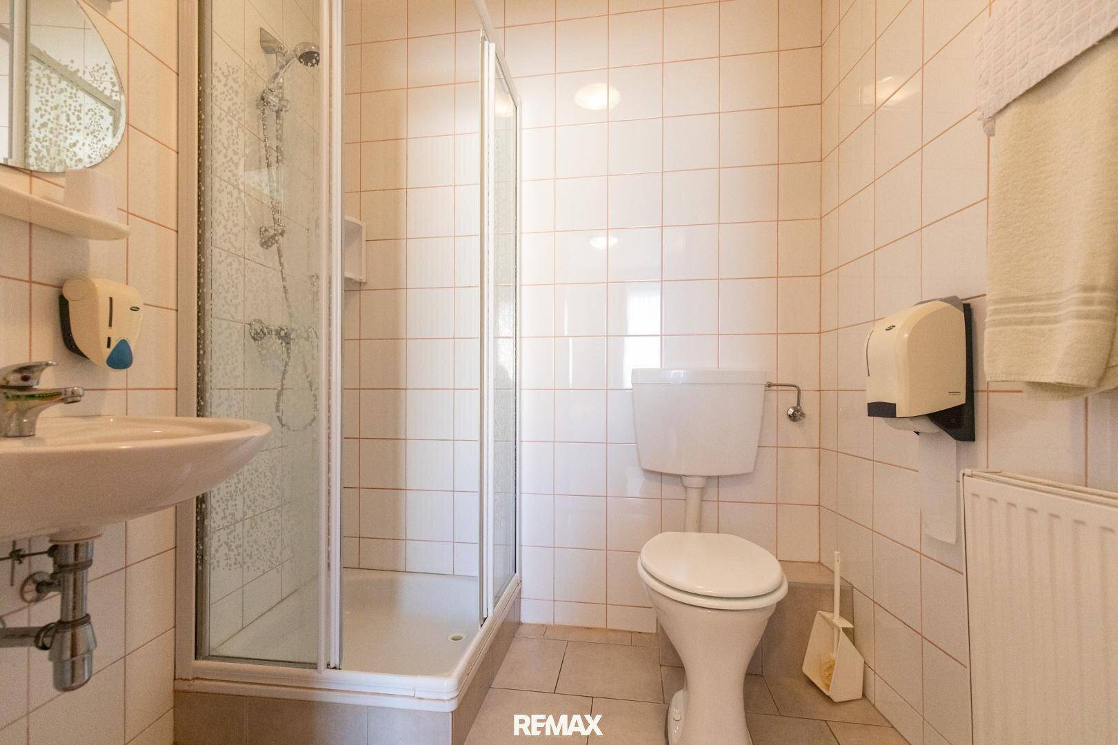 Helles Badezimmer mit Duschkabine, WC und Waschbecken, komplett gefliest in Beige.