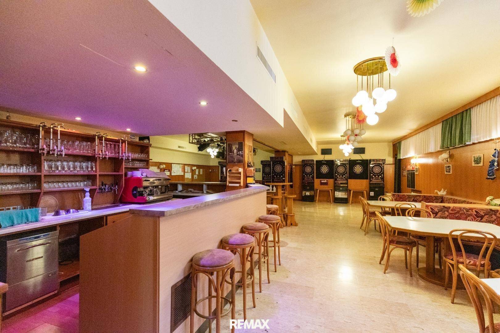Bar- und Unterhaltungsbereich mit Dartscheiben, Tischen und einer Theke mit Beleuchtung.