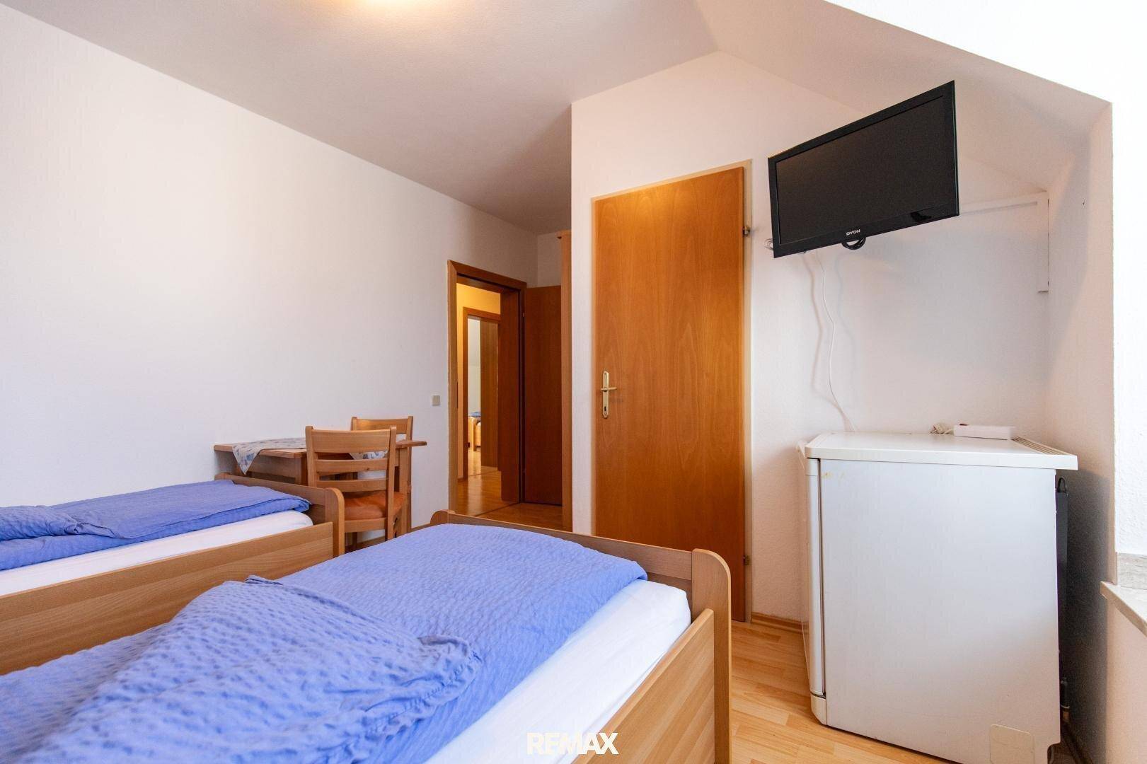Schlafzimmer mit zwei Einzelbetten, kleinem Kühlschrank und einem Wandfernseher unter der Dachschräge.