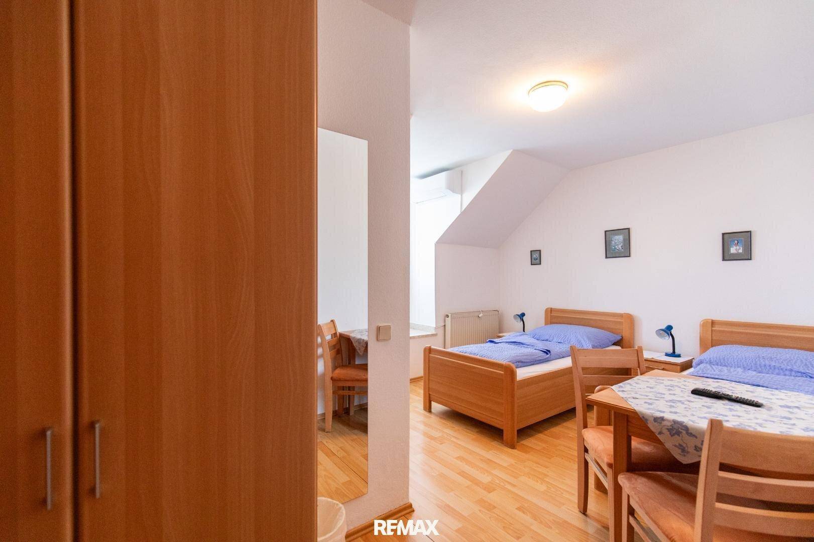 Schlafzimmer mit zwei Einzelbetten, Holzschrank und einem Tisch, unter einer Dachschräge gelegen.