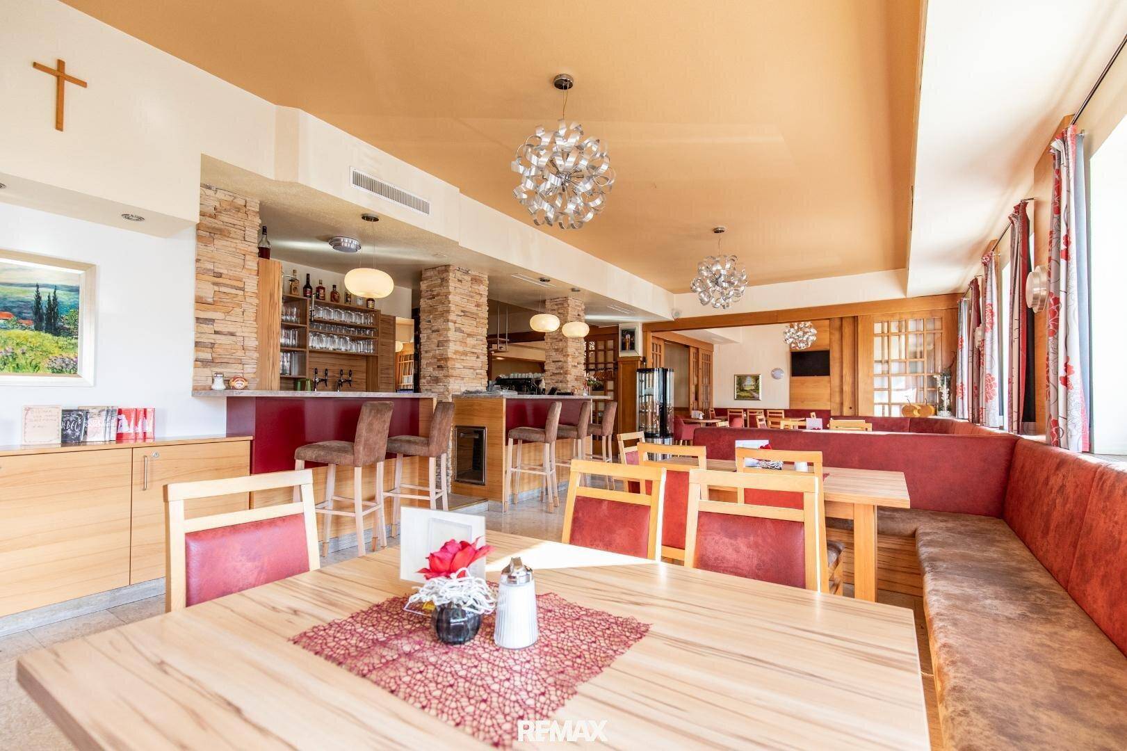 Geräumiger Speisesaal mit Holztischen, gepolsterten Bänken und einer Bar mit Steinverkleidung.