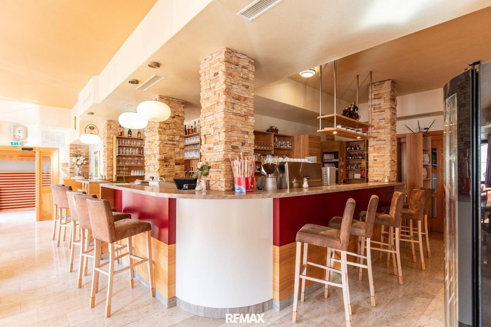 Detailansicht der Bar im Restaurant mit Steinverkleidung, Barhockern und Regalen für Gläser.