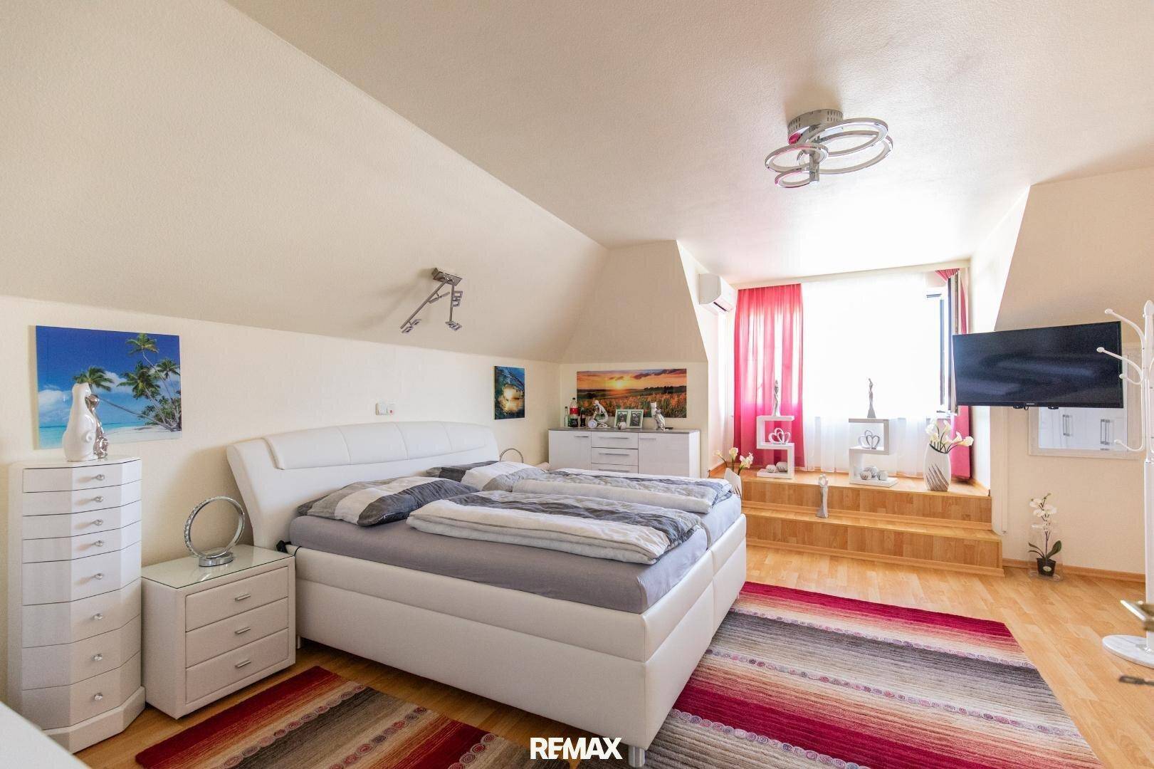 Helles Schlafzimmer im Dachgeschoss mit Doppelbett, modernen Möbeln und einem erhöhten Fensterbereich.