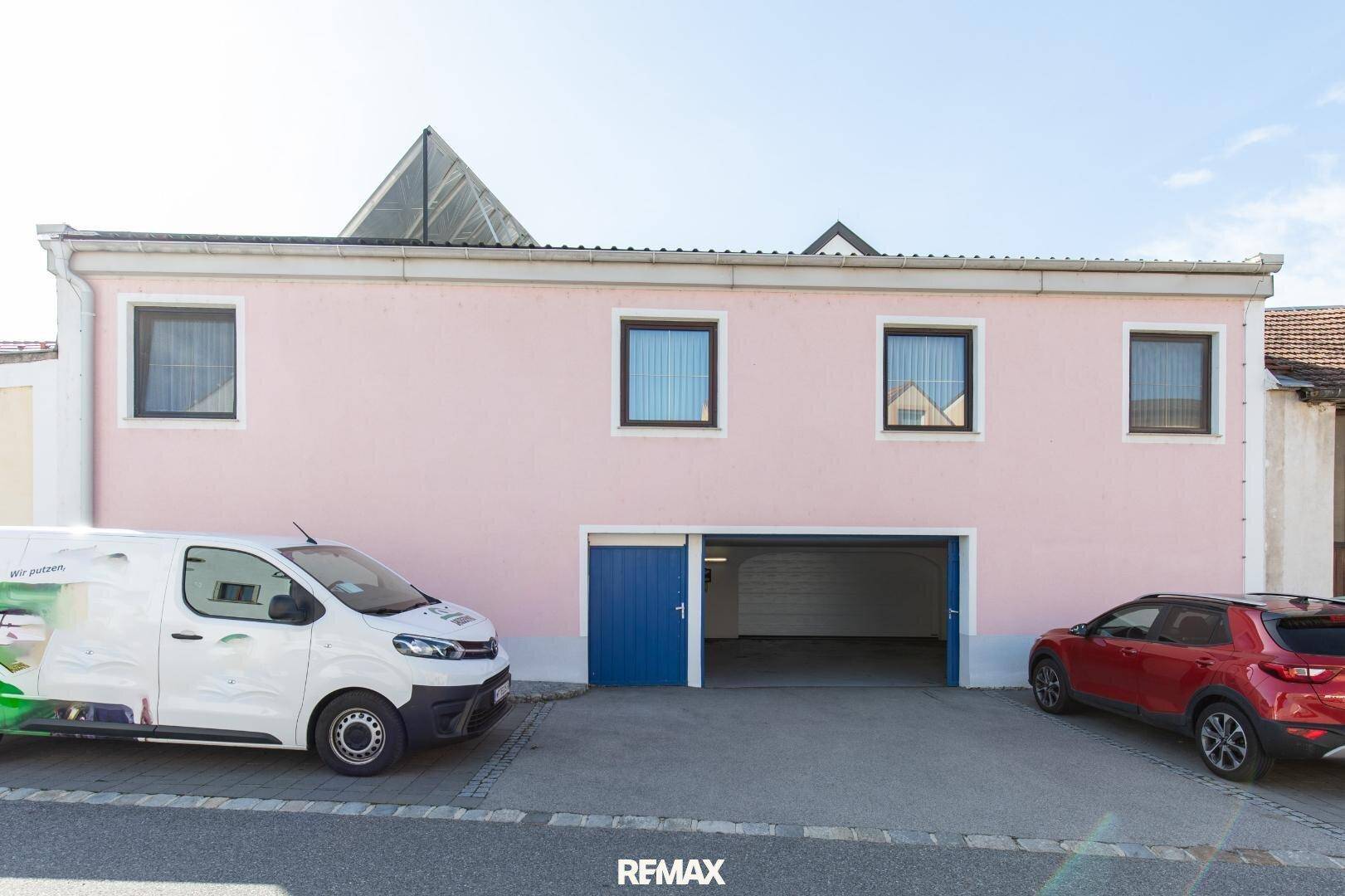 Rückseite des Gebäudes mit rosa Fassade, mehreren Fenstern und einer Doppelgarage.
