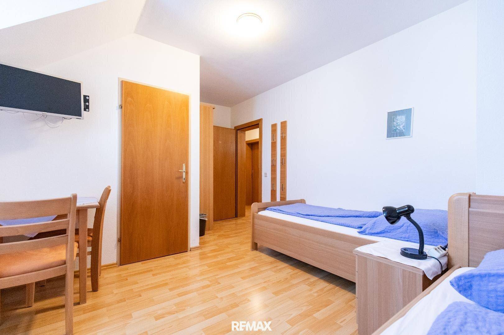 Helles Schlafzimmer mit zwei Einzelbetten, Holzboden und einem kleinen Tisch mit Stühlen.