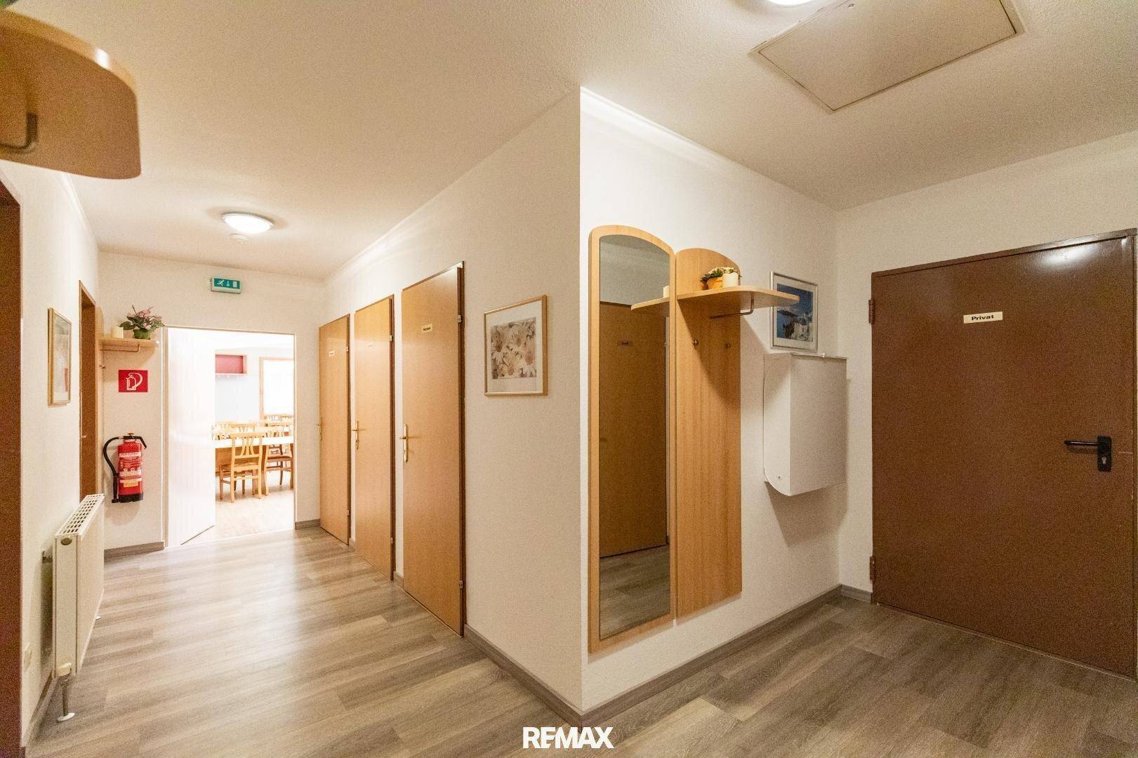 Heller Flur mit mehreren Holztüren, Garderobe und einem Feuerlöscher an der Wand.